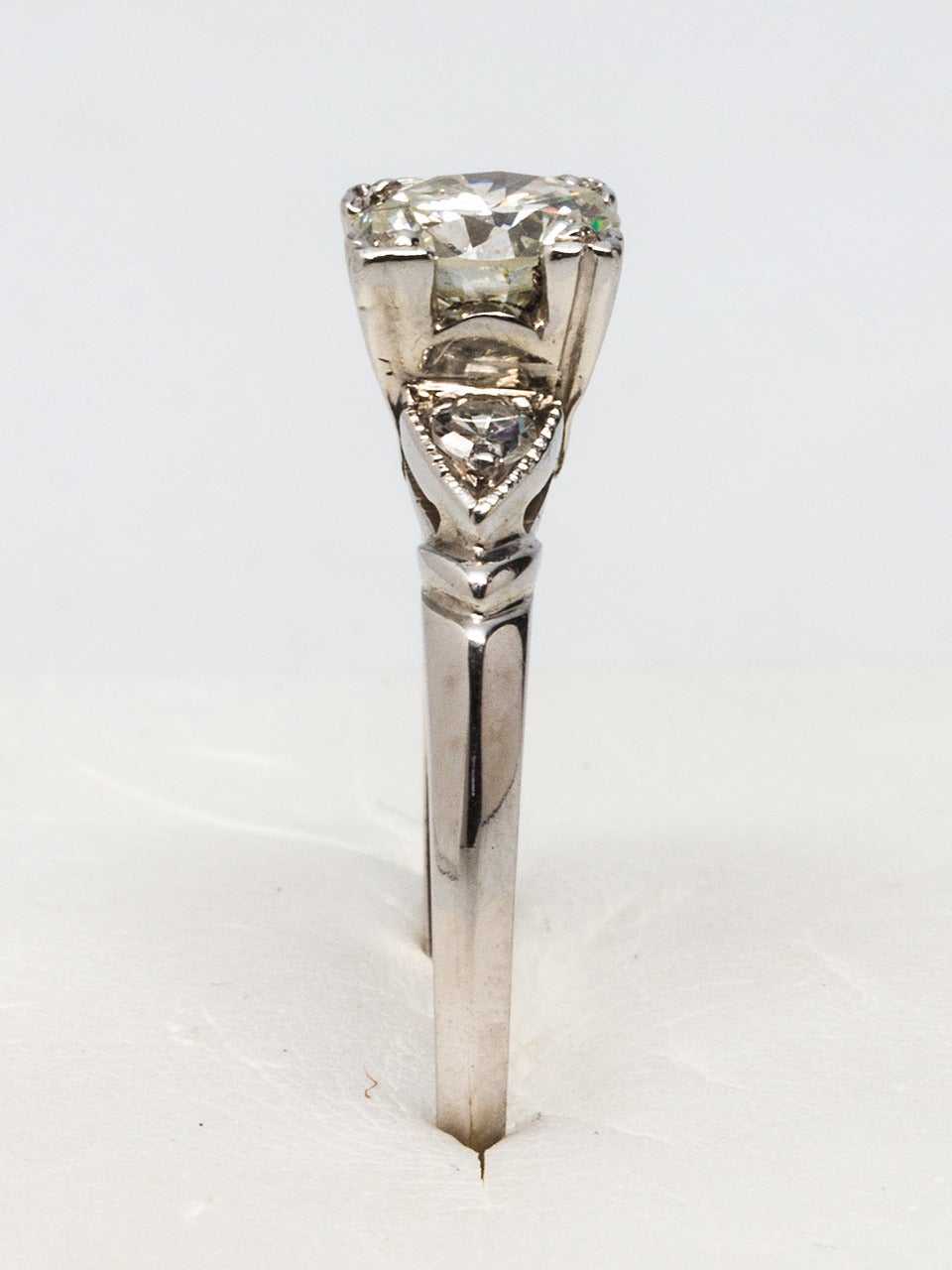 Platinum setting featuring an approximately 0.85 carat Round Brilliant Cut diamond, J color and SI2 clarity. Flanked by two single cut side stones in triangular settings, sculpted detail on shank. Size 6 Circa 1950s.

As a special offering for our