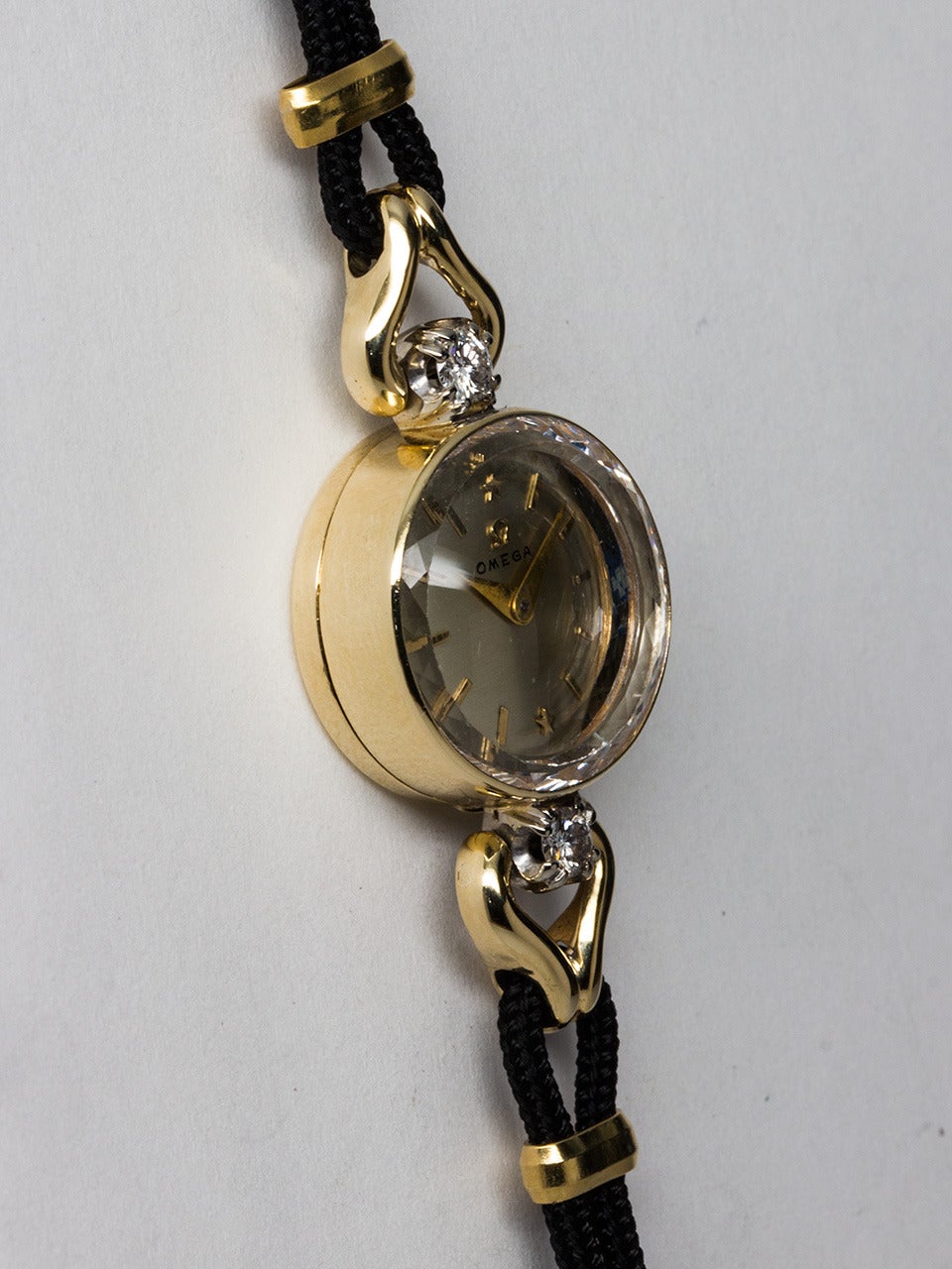 Lady Omega 14K Yellow Gold and Diamond Wristwatch circa 1950s. Diamond set round case 17 X 17mm with wish bone lugs. Original silvered satin dial with gold applied indexes, applied gold Omega logo and tapered sword hands. Shown on black silk and