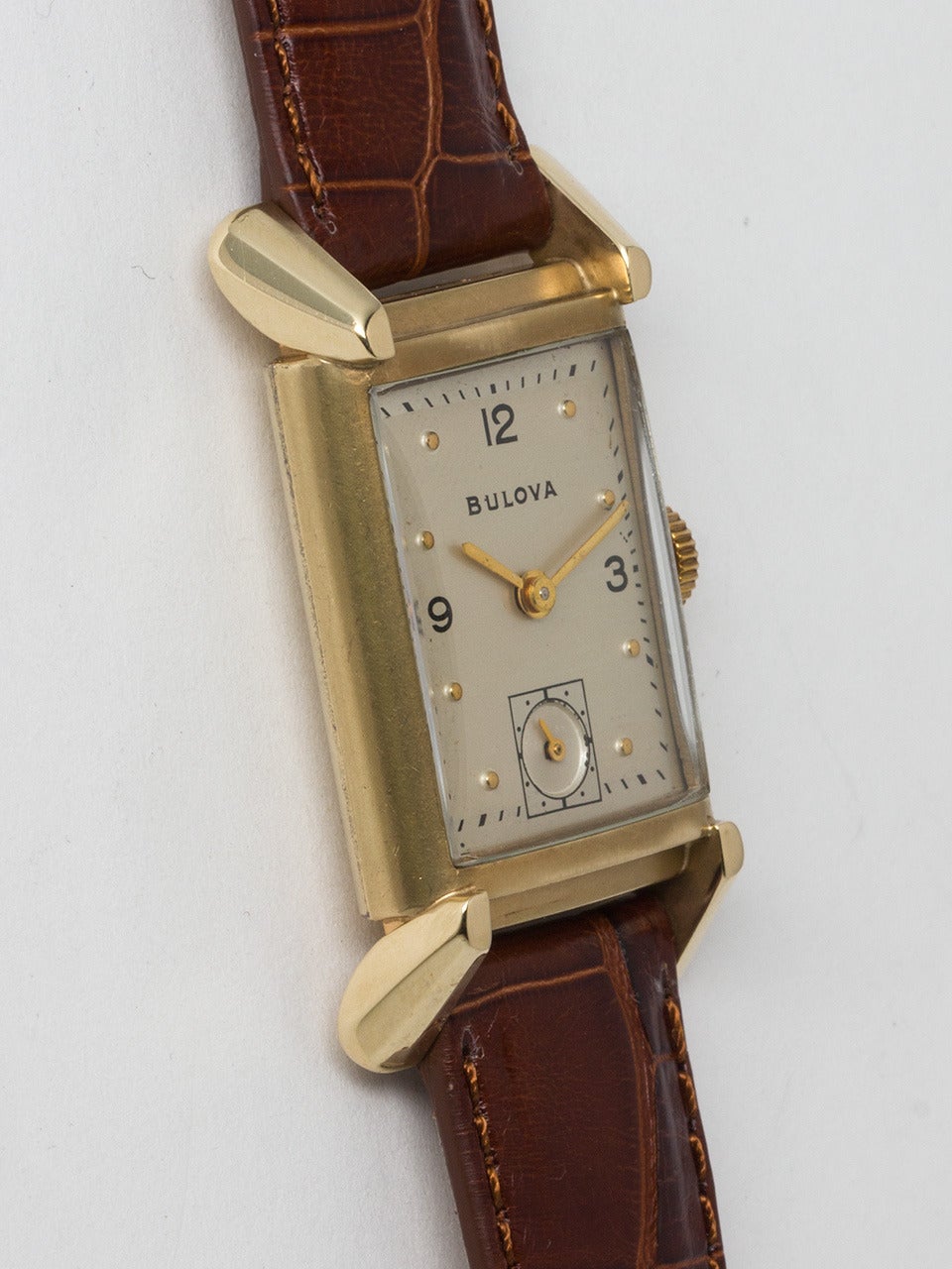 Bulova 14K Yellow Gold Rectangular Dress Watch, circa 1950s. Stylish case measuring 22 X 39mm with large sloped footed lugs. Original silvered satin dial with gold raised dots and printed 3, 9 and 12. Powered by 17 jewel manual wind movement with