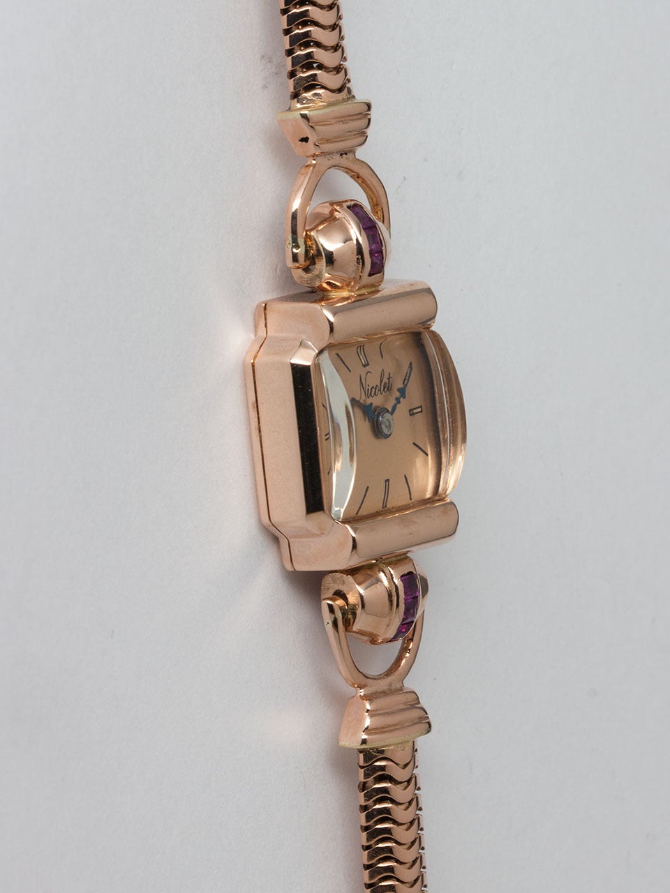 Nicolet Swiss 14K Rose Gold Lady's Dress Wristwatch circa 1940s. Square case 15 x18mm with 6 rubies on stylized lugs. With salmon dial with blue steeled hands. Powered by manual wind movement. Personalized name on case back. Heavy 14K rose gold