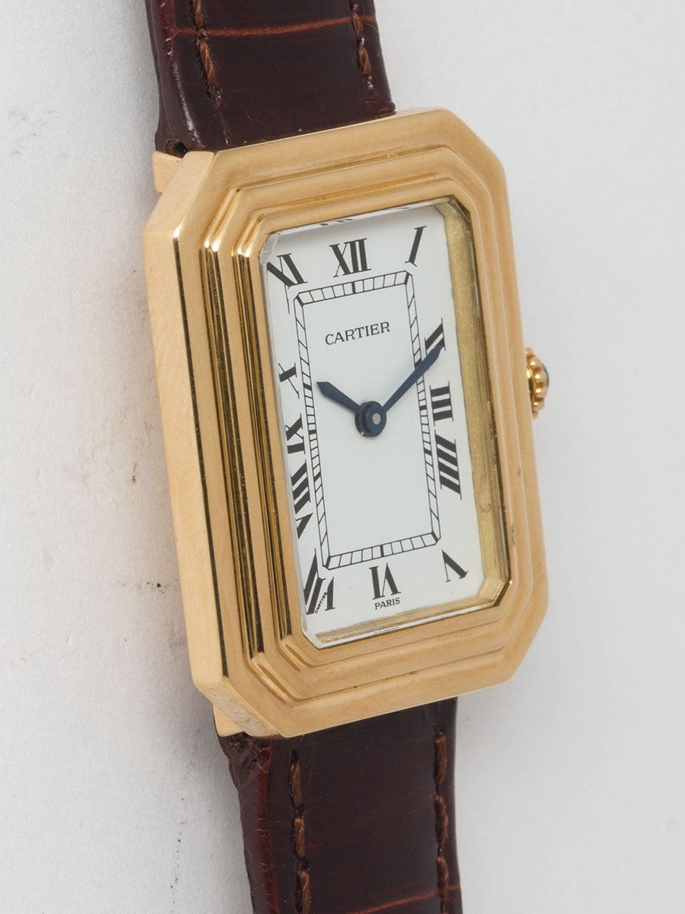 Cartier 18K Yellow Gold Cristallor Tank circa 1973. Featuring stepped sculpted 24 X 30mm rectangular case with cut corners and cabochon sapphire crown. With classic white dial with printed black Roman figures and blued steel hands. Powered by 17