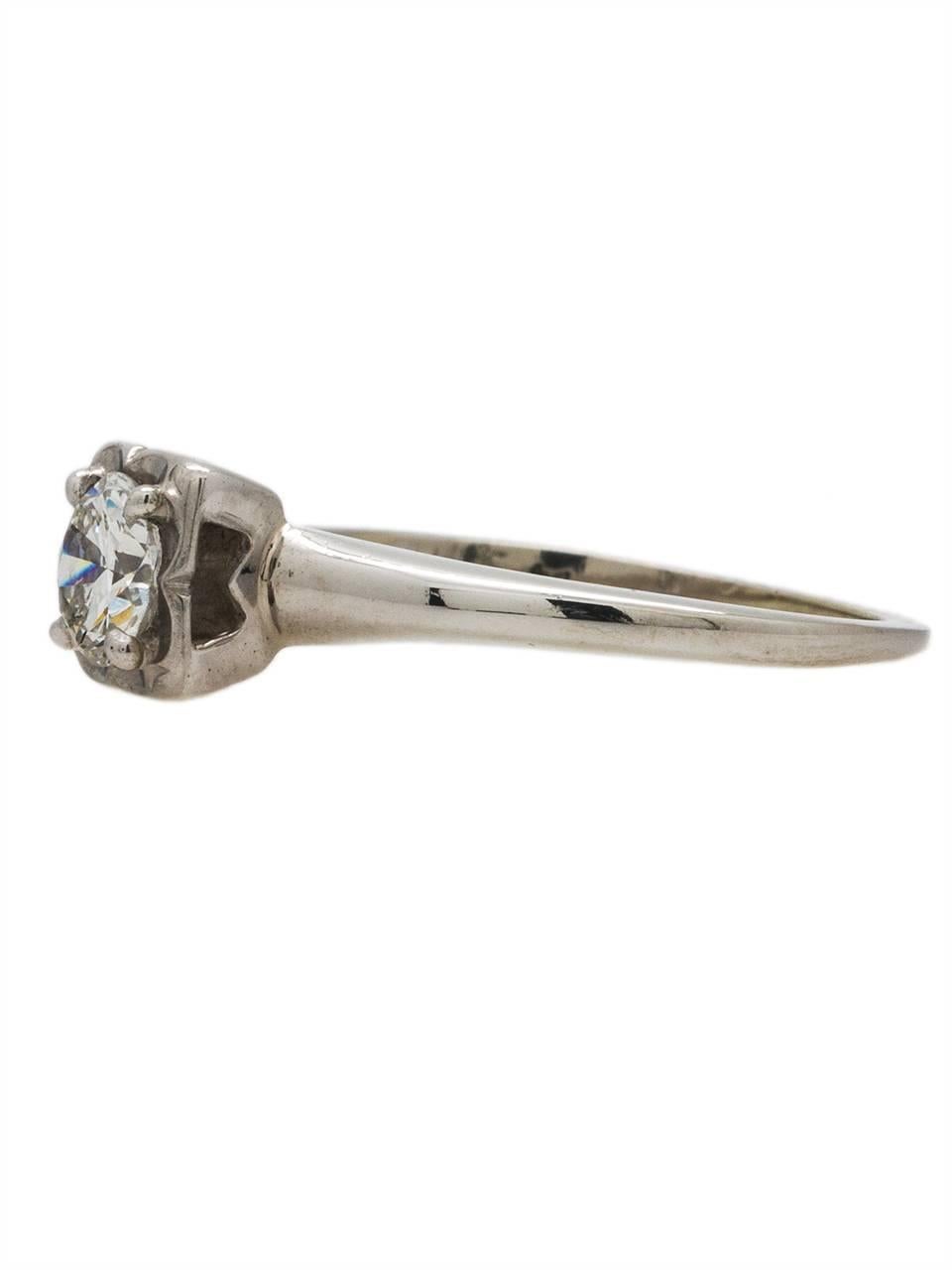 This simple solitaire engagement ring in 14k white gold is set with a brilliant 0.40ct modern round cut diamond, G/SI1. The elevated mounting has a romantic geometric Art Deco cutout gallery with ridge detail. An elegant tulip flower illusion