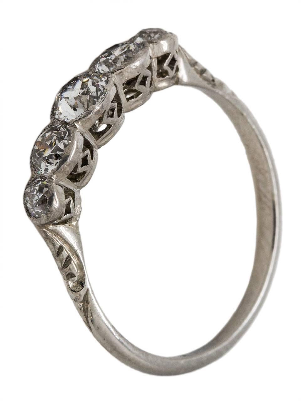 This lovely platinum diamond band is a wonderful example of Edwardian design with its intricately detailed elevated settings and romantic engraving down the sides of the shank. Each bright and lively Old European Cut diamond is bezel set and exhibit