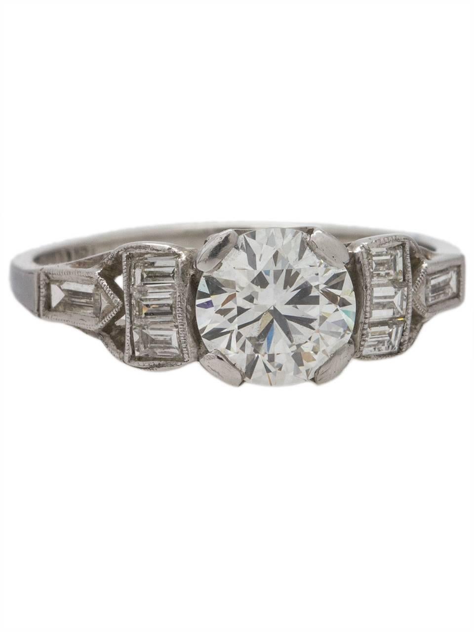 This vintage Art Deco platinum engagement ring features a lively 1.03 carat round brilliant cut diamond, E/VS2. The center stone is set almost flush with eight straight baguette cut side stones, giving this beauty a fantastic lower profile