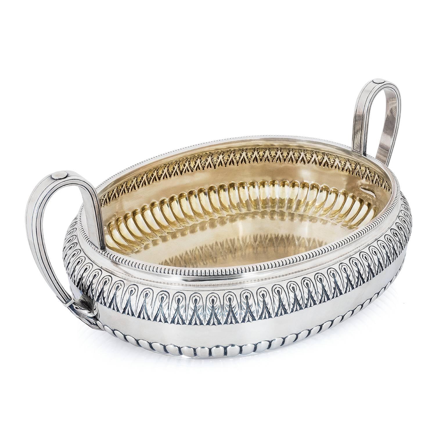A silver fruit bowl by Fabergé, on short straight foot, oval-shaped, with rounded body and beaded outer rim, the lower section fluted, the upper section chased with an ornate pattern band of foliate motif, a pair of ribbon-shaped vertical handles
