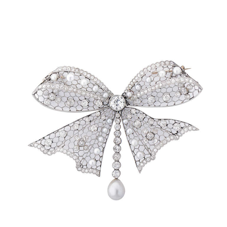 An archetypal Edwardian platinum bow brooch, comprising of 20 natural pearls and approximately 5cts of diamonds, including the principal round stone in the centre, weighing 0.7cts. Circa 1910. In a fitted box.

The brooch is 65mm wide at its