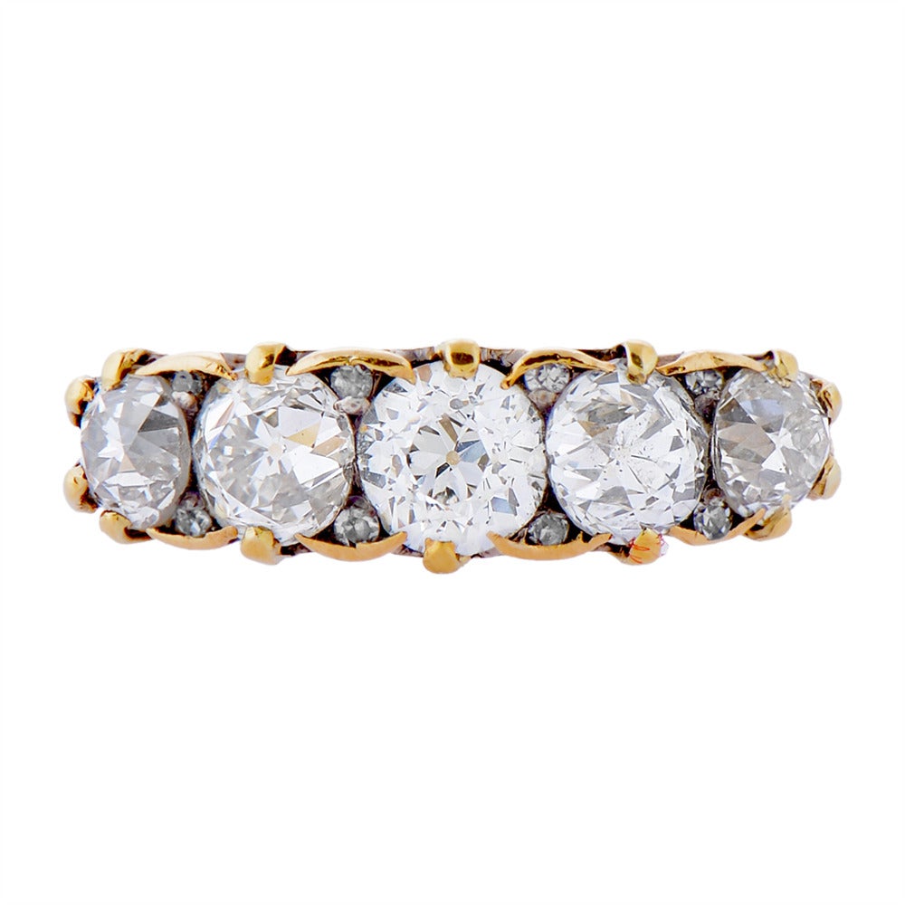 A Victorian five stone diamond ring set in yellow gold composed of five old-cut diamonds of approximately 3cts, graduated in size from the centre, with diamond points between them and a scroll carved gallery. Estimated colour L–M and VS–SI clarity.