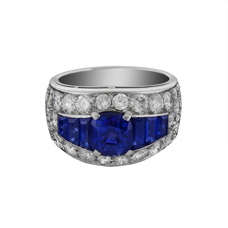 A sapphire and diamond ring by Bulgari, the central cushion shaped sapphire, weighing 2.67 carats, in a four claw setting, between calibre cut sapphires, within a bombe shaped surround set throughout with brilliant cut diamonds, approximately 2.18