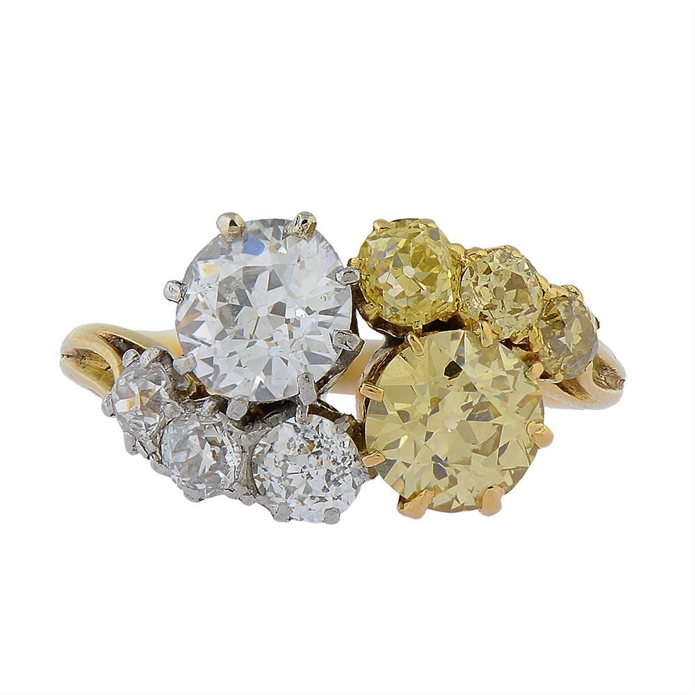 A gold, fancy yellow diamond and white diamond crossover ring, centring on two larger old-cut diamonds, one fancy yellow and one white, framed by three smaller diamonds, gradated in size, of each colour, all mounted in yellow gold. The fancy yellow