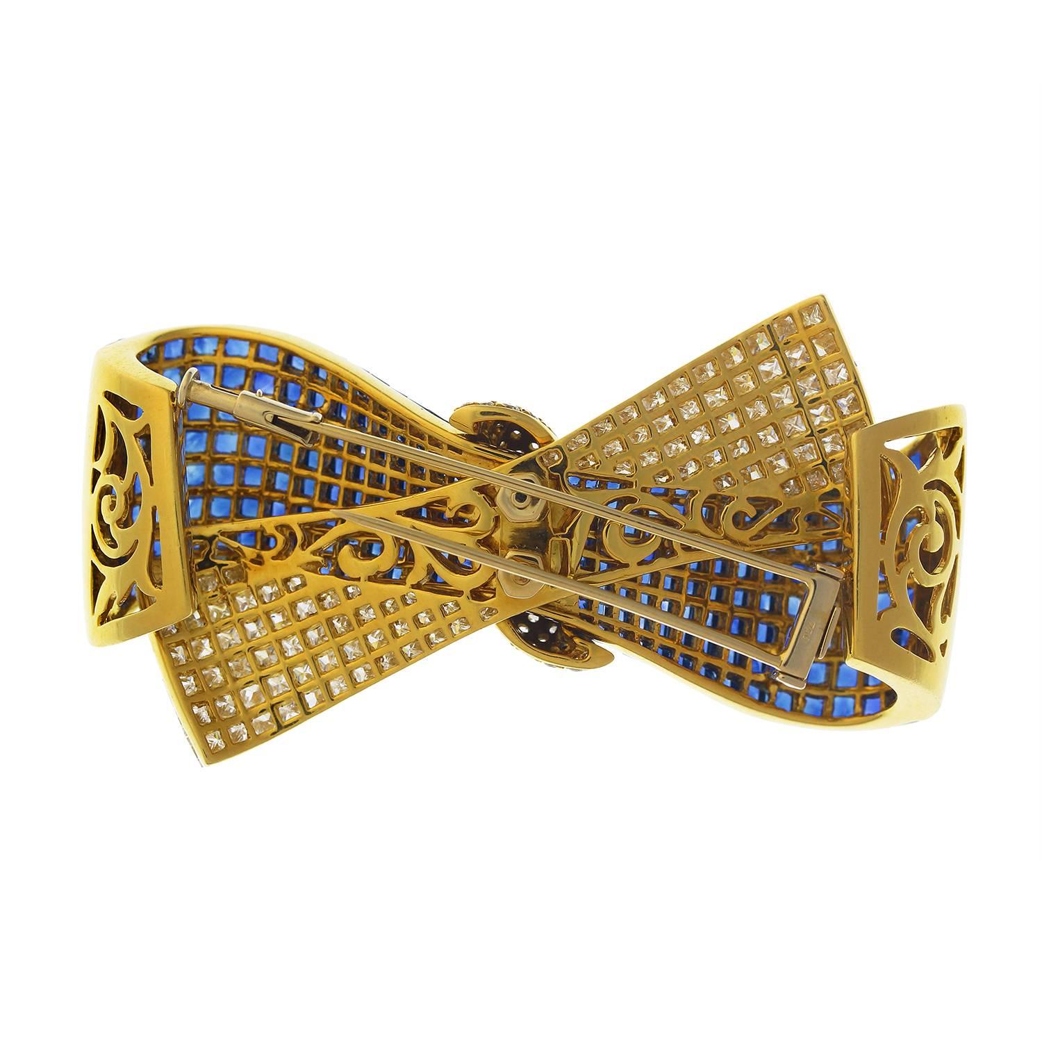 A gold sapphire and diamond bow brooch, the ribbon front invisibly set with calibré-set graduated sapphires & princess-cut diamonds, with bombé centre, pavé-set with brilliant-cut diamonds, marked 750 for 18KT gold. Approximately 6.5 cm (W) by