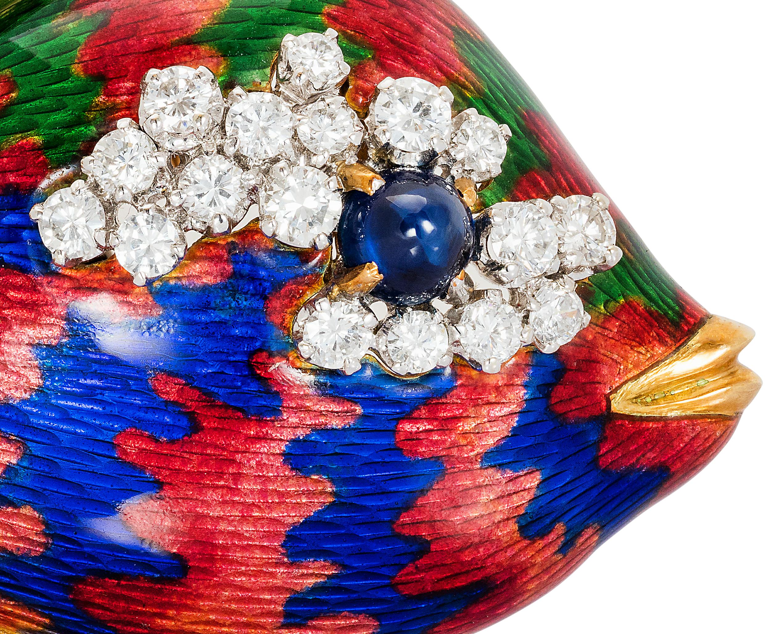 A whimsical fish brooch, fins and mouth made in carved yellow gold, body decorated with red, blue and green enamel. Cabochon sapphire eye surrounded by a cluster of diamonds. Circa 1970s.