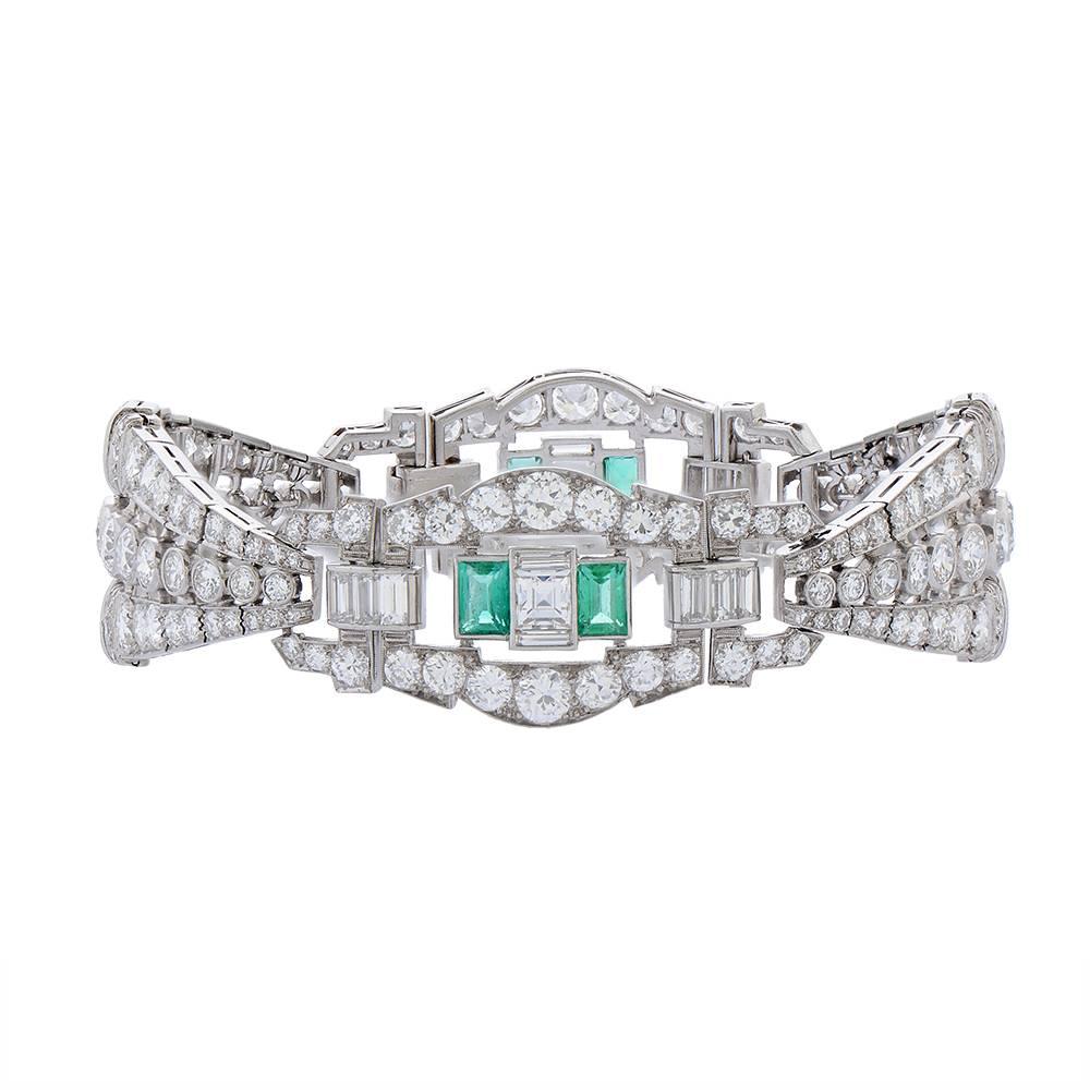 A platinum, diamond and emerald bracelet, composed of articulated lozenge-shaped and openwork links, set with round, baguette and square-cut diamonds and flashes of emerald-cut emeralds, each lozenge-shaped link framing a row of round-cut diamond