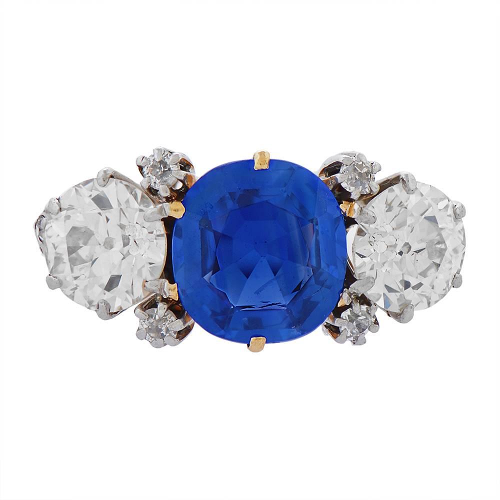 A gold and platinum, Kashmir sapphire and diamond ring by J.E. Caldwell, a cushion-cut 2.71ct blue sapphire at its centre, framed at four corners by small diamond accents and flanked on either side by a round old-cut diamond, weighing a total of