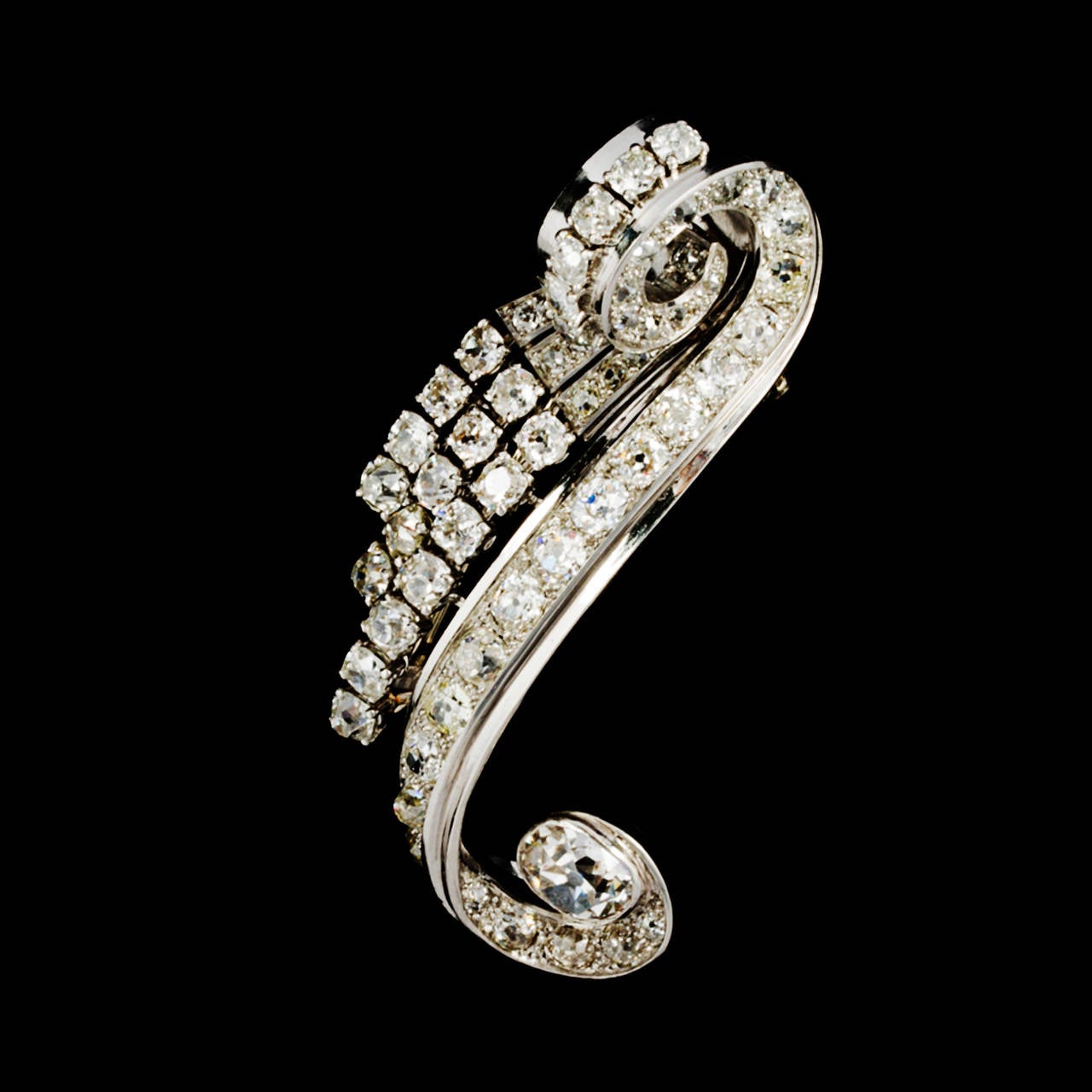(950°/oo) platinum and 18ct (750°/oo) white gold Dress clip brooch ornated with a scrolling band set with old-mine cut diamonds and ended by a cushion shape diamond approximately weighing 1.80ct. 

Three lines of graduated old-mine cut diamonds on