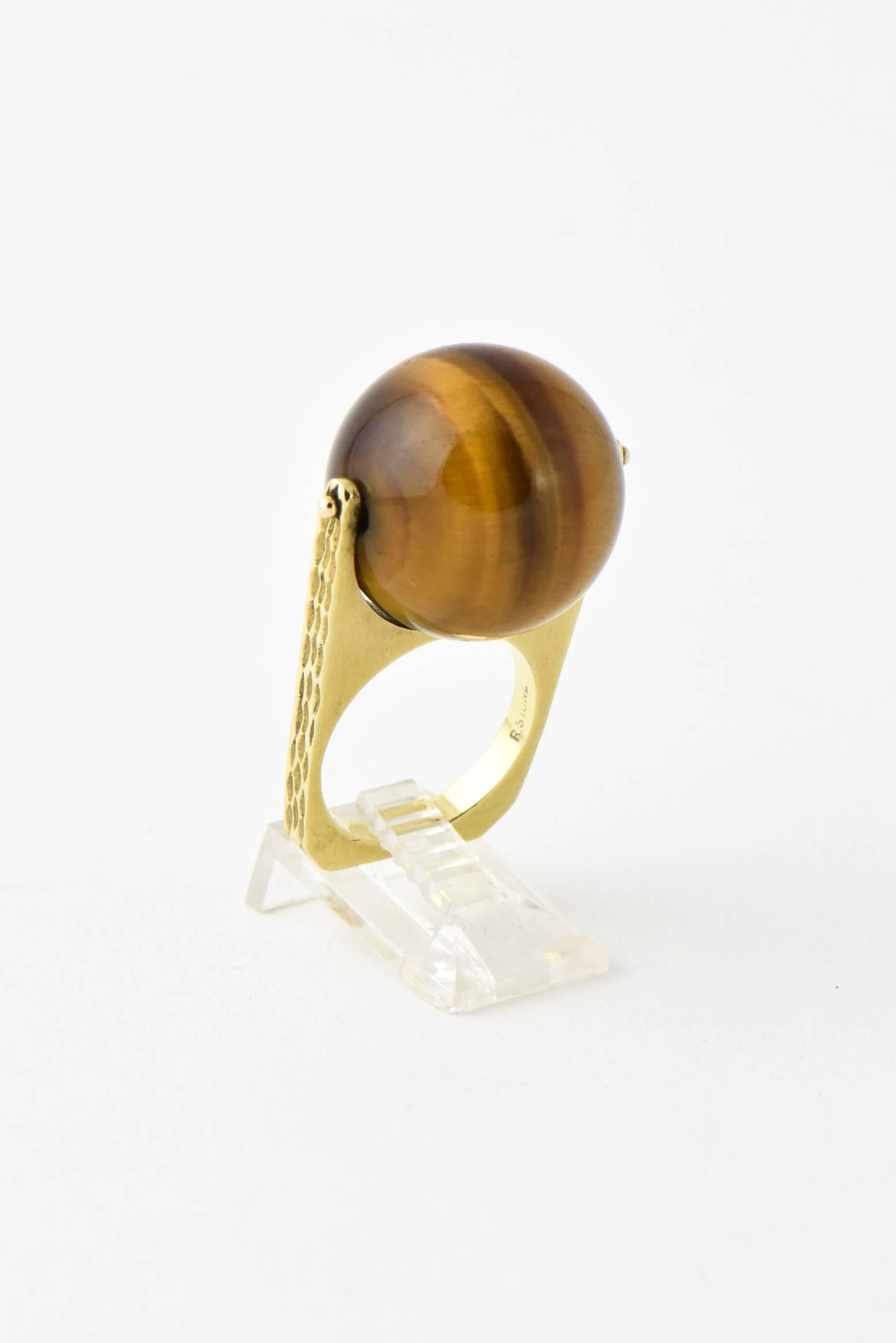 Cool 1960's Ball Ring featuring a 18k yellow gold rectangular ring with bark finish sides holding a large 20mm tiger's eye ball that spins by New York jeweler, R. Stone. 

US size 6.25 

Marked 18k R. Stone

