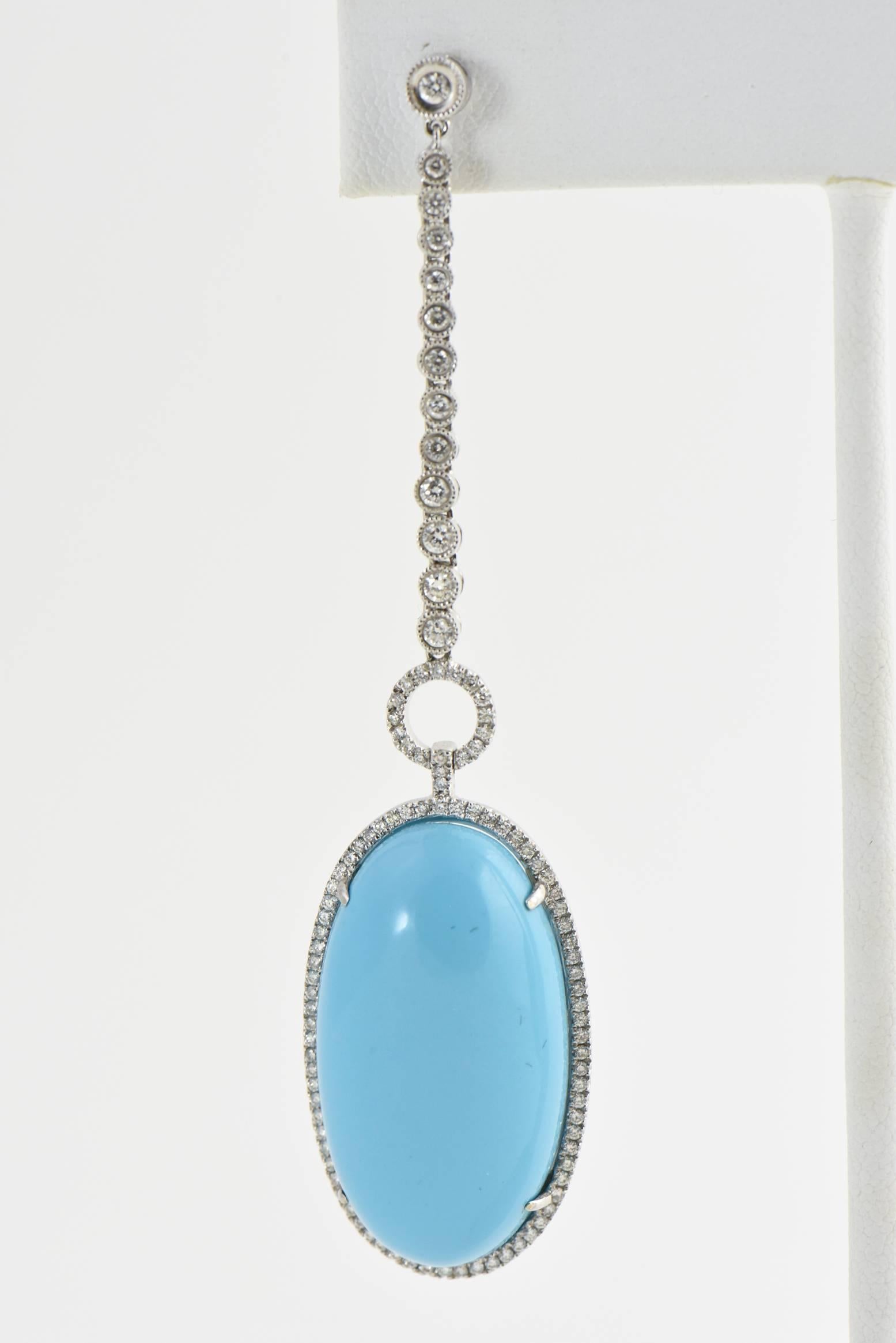 Featuring 2 large oval cabochon pieces of reconstituted turquoise mounted in diamond frames that are attached to a diamond ring that hangs from 12 graduating in size diamonds in a beaded bezel mount that attaches to a matching small diamond stud. 