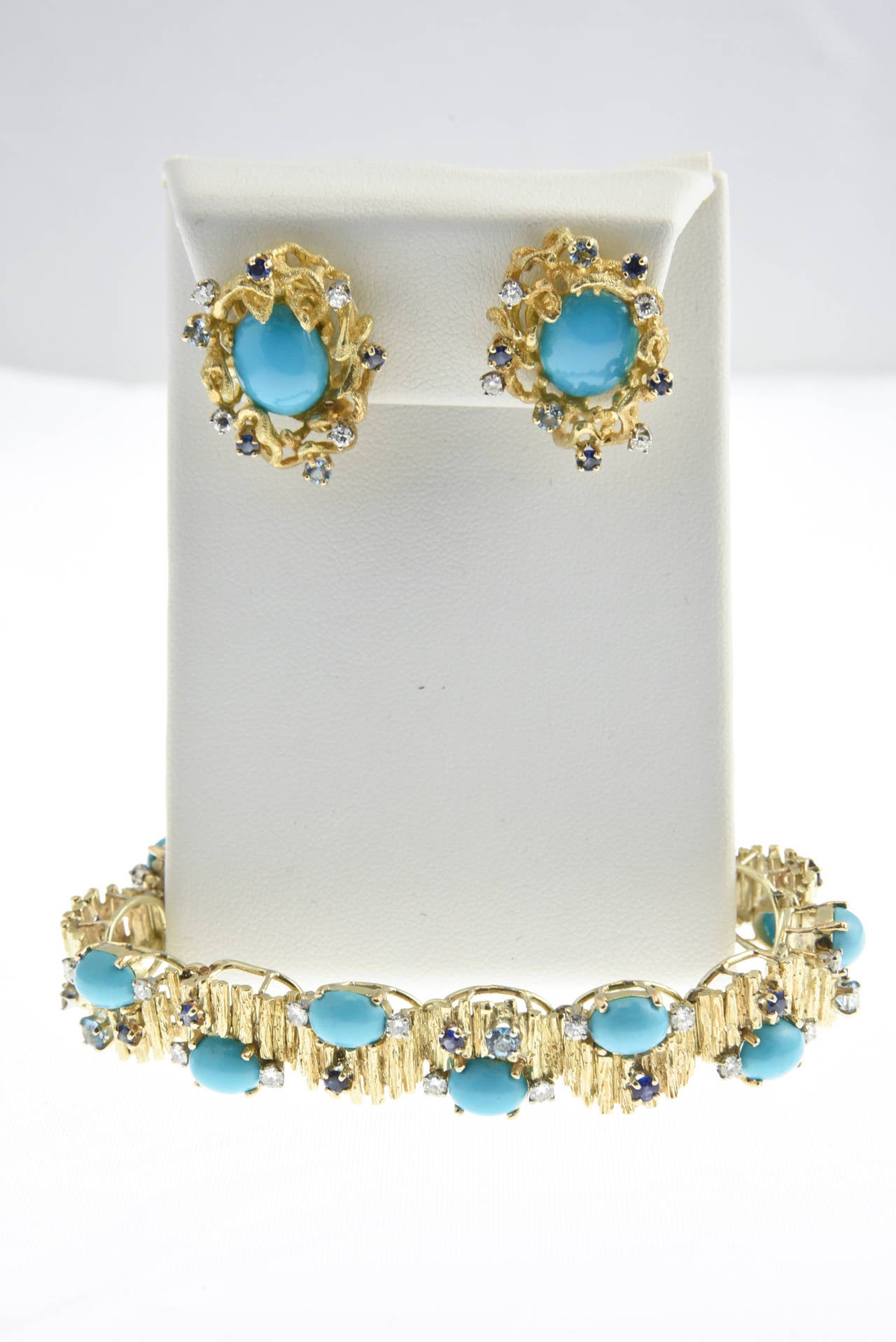 This wonderful 1960's set by Jack Gutschneider includes a bracelet with bark finish links accented by cabochon turquoise pieces and facetted sapphires, blue topaz and diamonds mounted in 14k yellow gold.

The earrings are clips with posts.  They