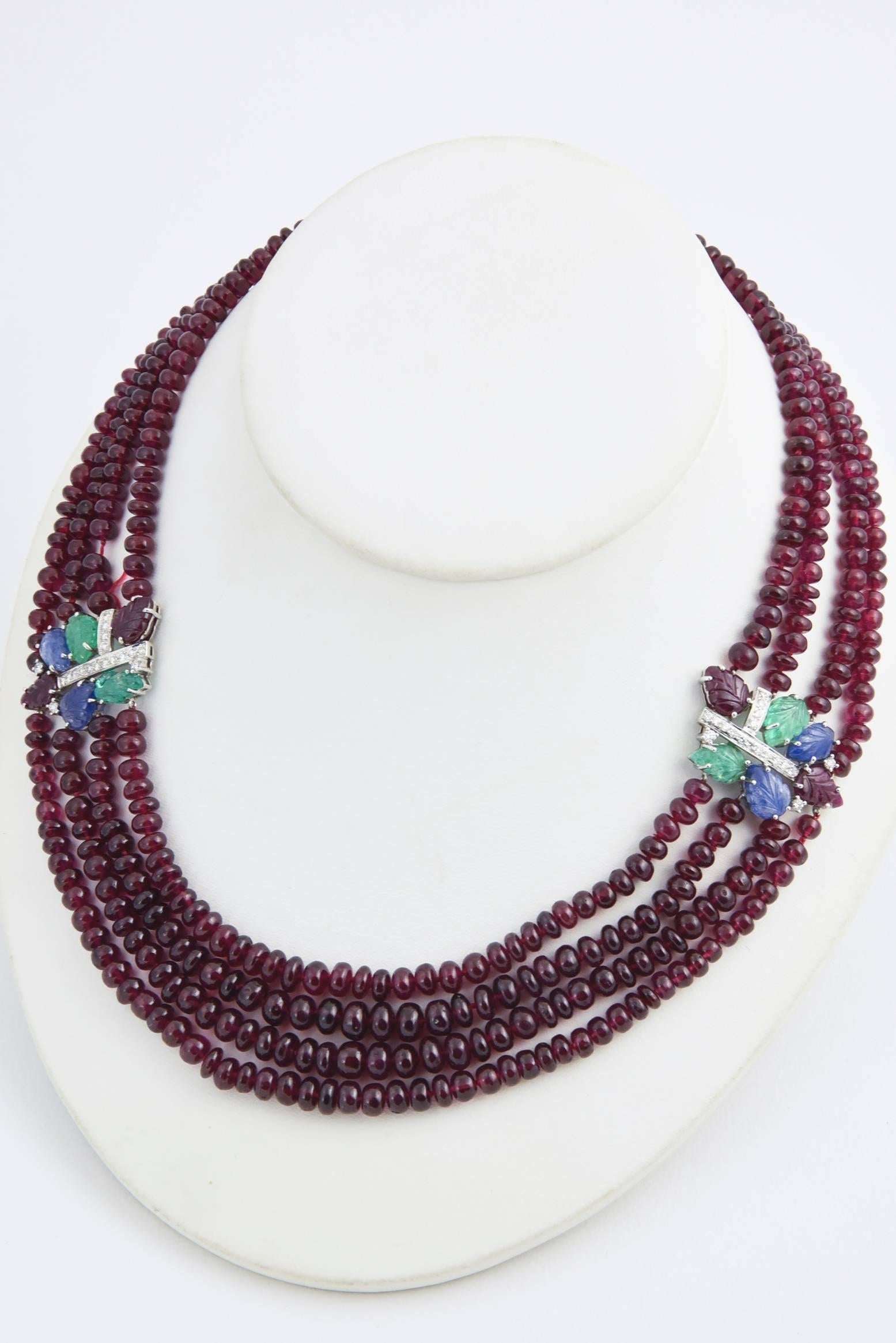 Impressive contemporary necklace containing four strands of ruby beads accented with two - 18k white gold tutti frutti spacers.  The spacers have carved ruby, emerald and sapphire leaves and diamonds.  At the back, there is a pave diamond 14k white