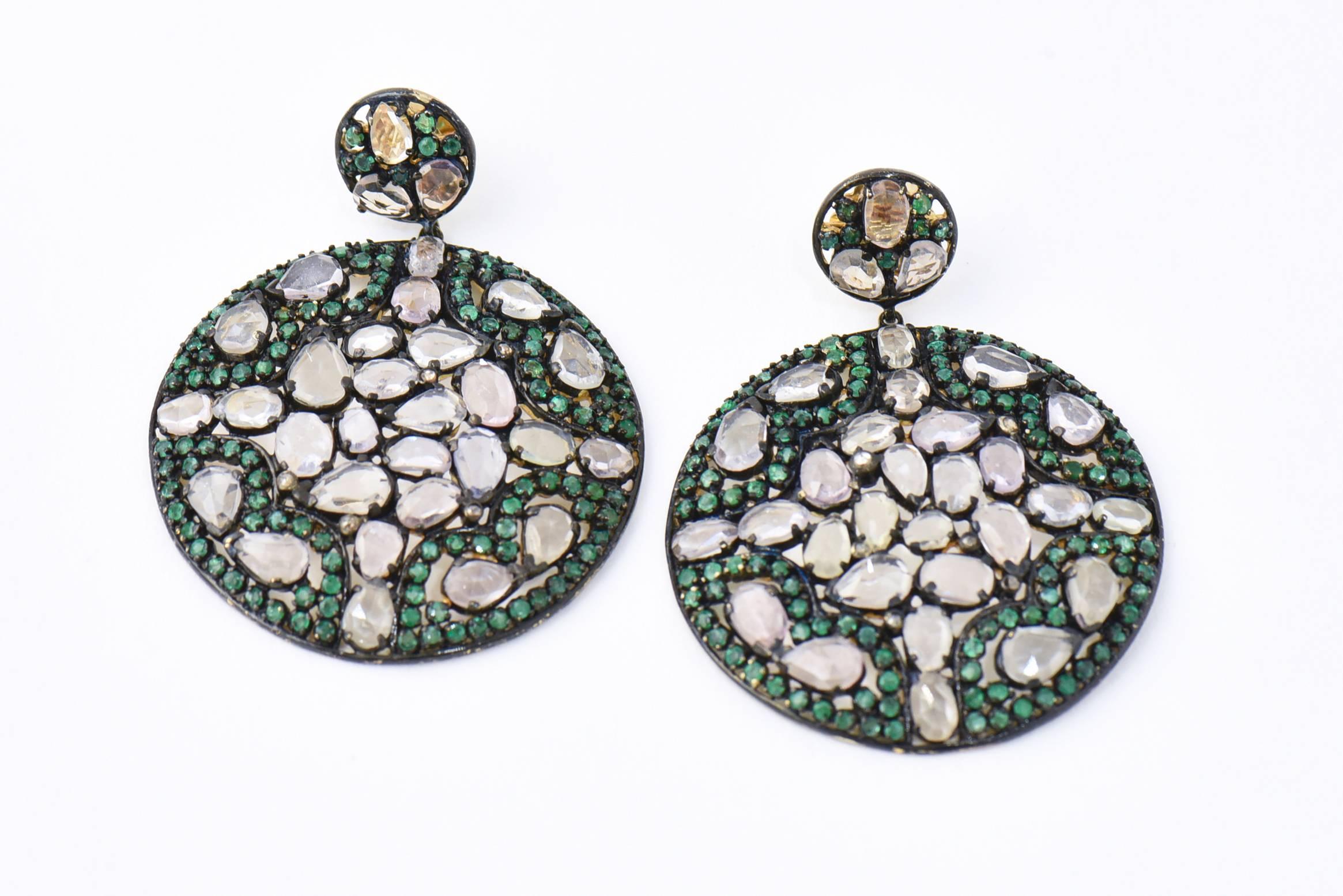 Lovely long dangling earrings that resemble a stained glass window. An tsavorite garnet and white topaz design is set through the ear with an 18k yellow gold post. The large round drop features translucent tsavorite and white topaz with diamond