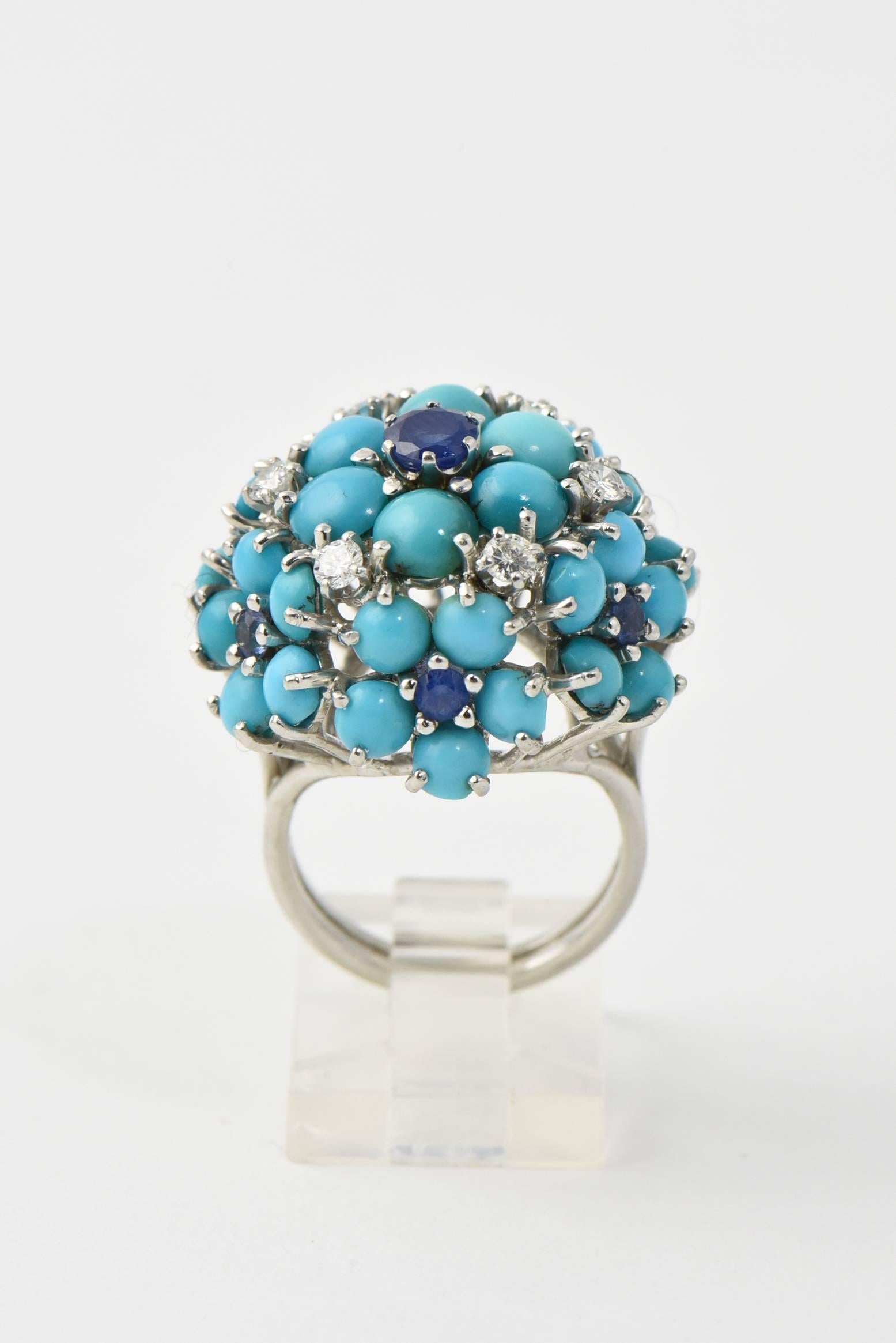 Turquoise flowers with sapphire centers and six interspersed prong set diamonds.  There is a larger flower in the center and six more flowers around the sides.  The ring is made of 14k white gold.

US size 6.5 - it can be sized.