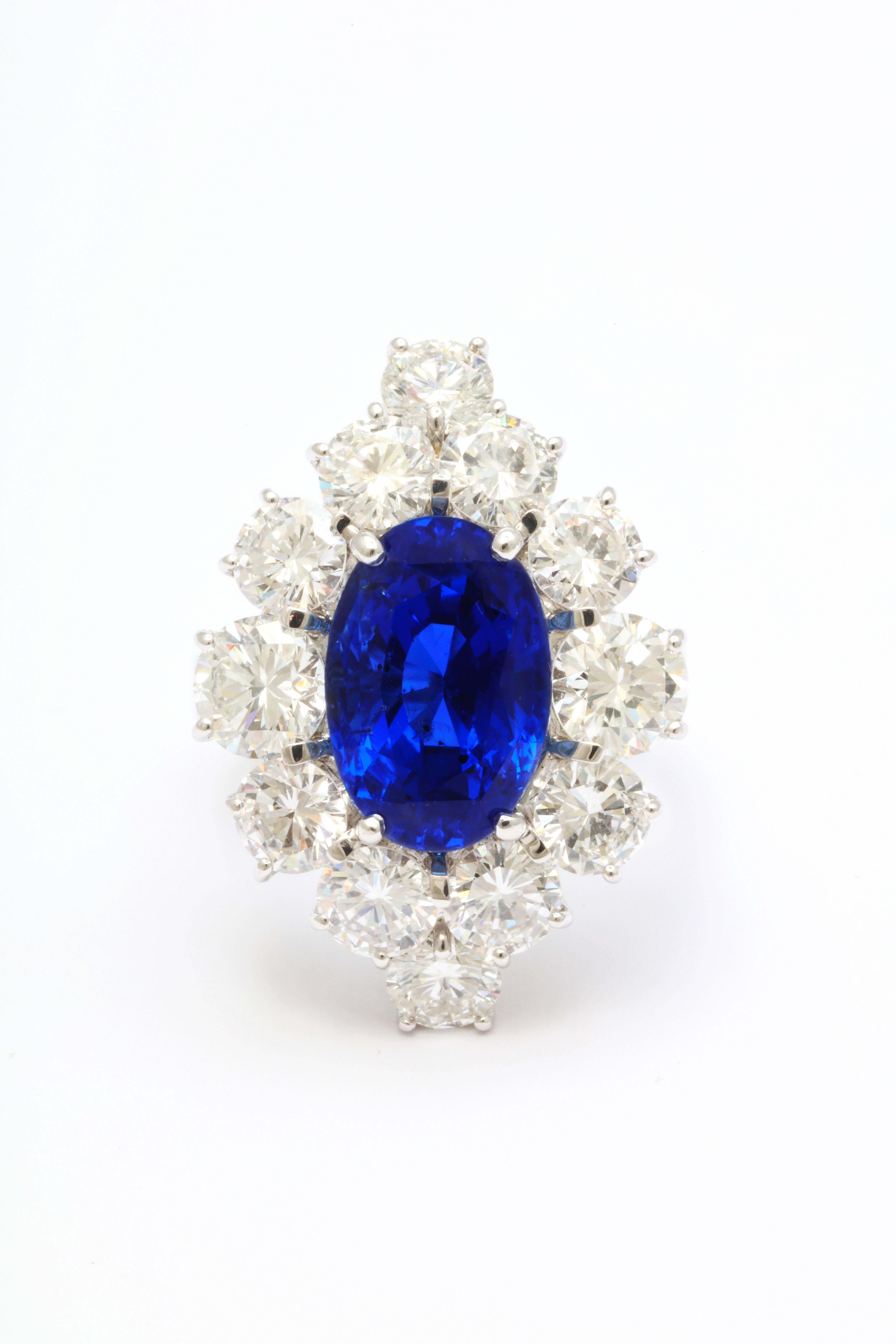 The bright blue app. 8.57 carat oval sapphire is surrounded by 12 round brilliant cut diamonds weighing 0.40 carats each.  The bright blue color of the sapphire, combined with the fantastic brilliance of the large, round diamonds results in a true