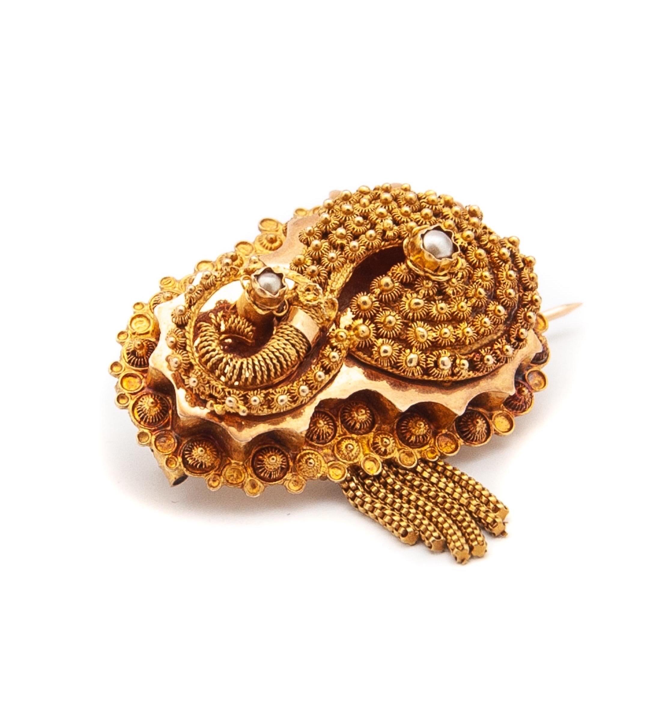 An antique cannetille brooch created in 14 karat yellow gold. The brooch is embellished with a texture of firm and fine lacy spiral gold thread and beading. Between the spiral cannetille knots, two seed pearls are placed and a gold spiral wire in