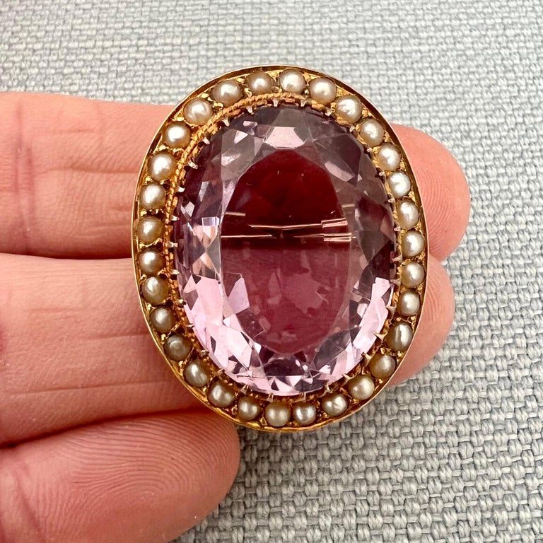 This late 19th century oval shaped openwork brooch is set with a large faceted amethyst. The amethyst is brilliant cut, translucent and has a beautiful purple levender color. Thirty creamy white seed pearls are inlaid in the gold frame around the