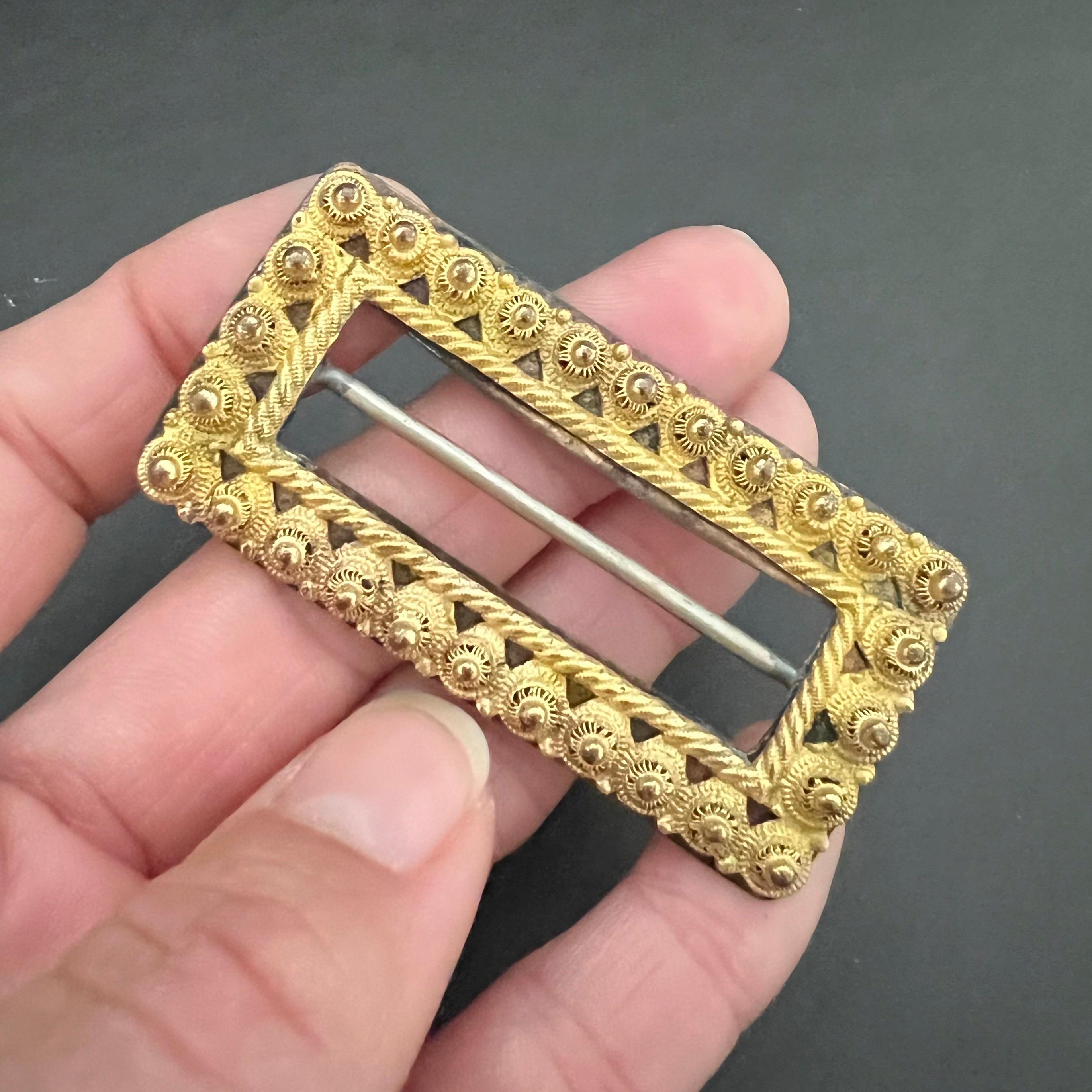 This antique 19th century filigree belt buckle is made of 10 karat yellow gold. The rectangular-shaped buckle is embellished with filigree knots and a rope motif. The top of the belt buckle is made of 10 karat yellow gold and the frame of the buckle