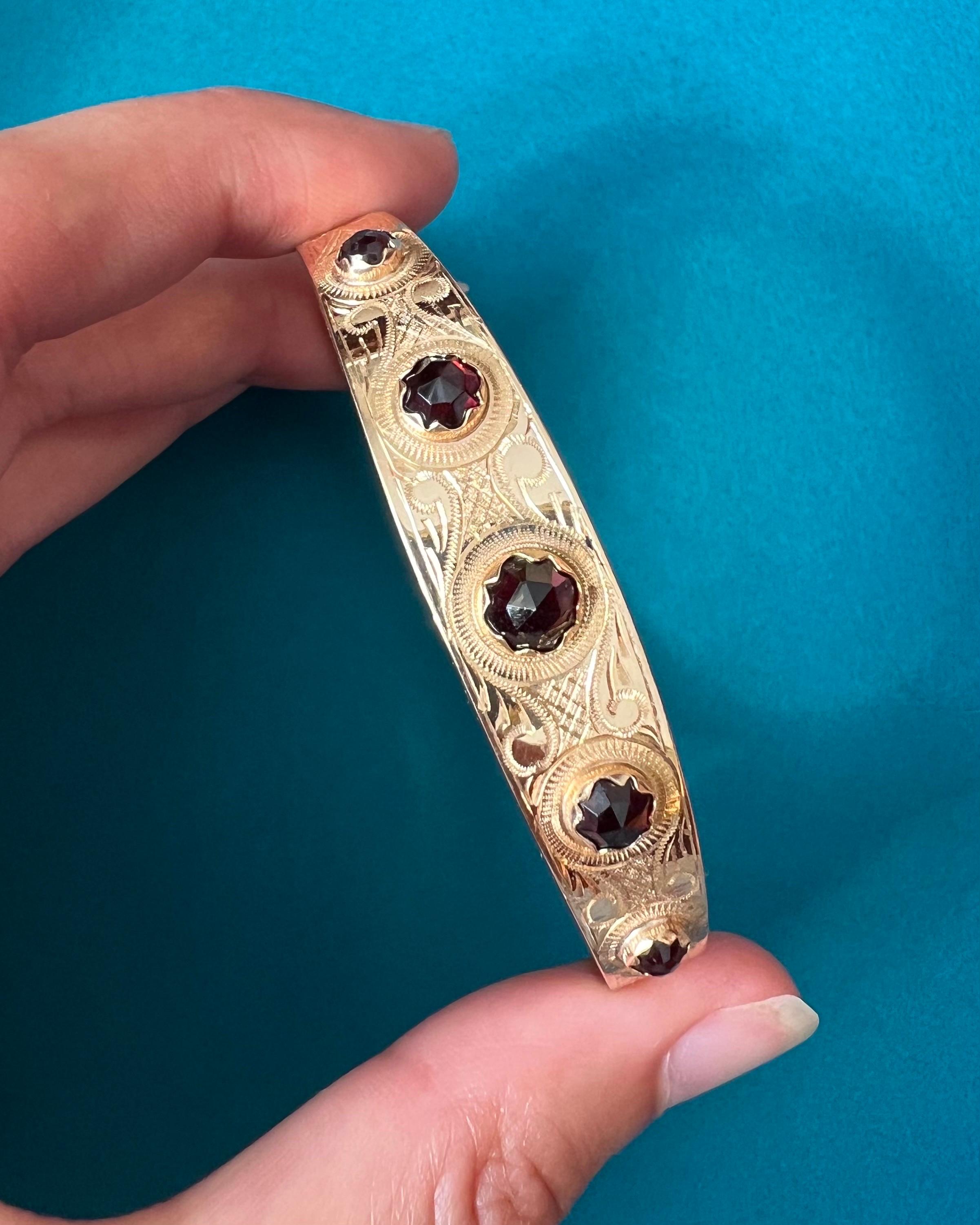 A vintage garnet bangle bracelet set in a 14 karat yellow frame. The gold of the bangle is beautifully made with an engraved and structured design. The bracelet features five faceted garnet stones set in a gold scalloped bezel setting. The garnets
