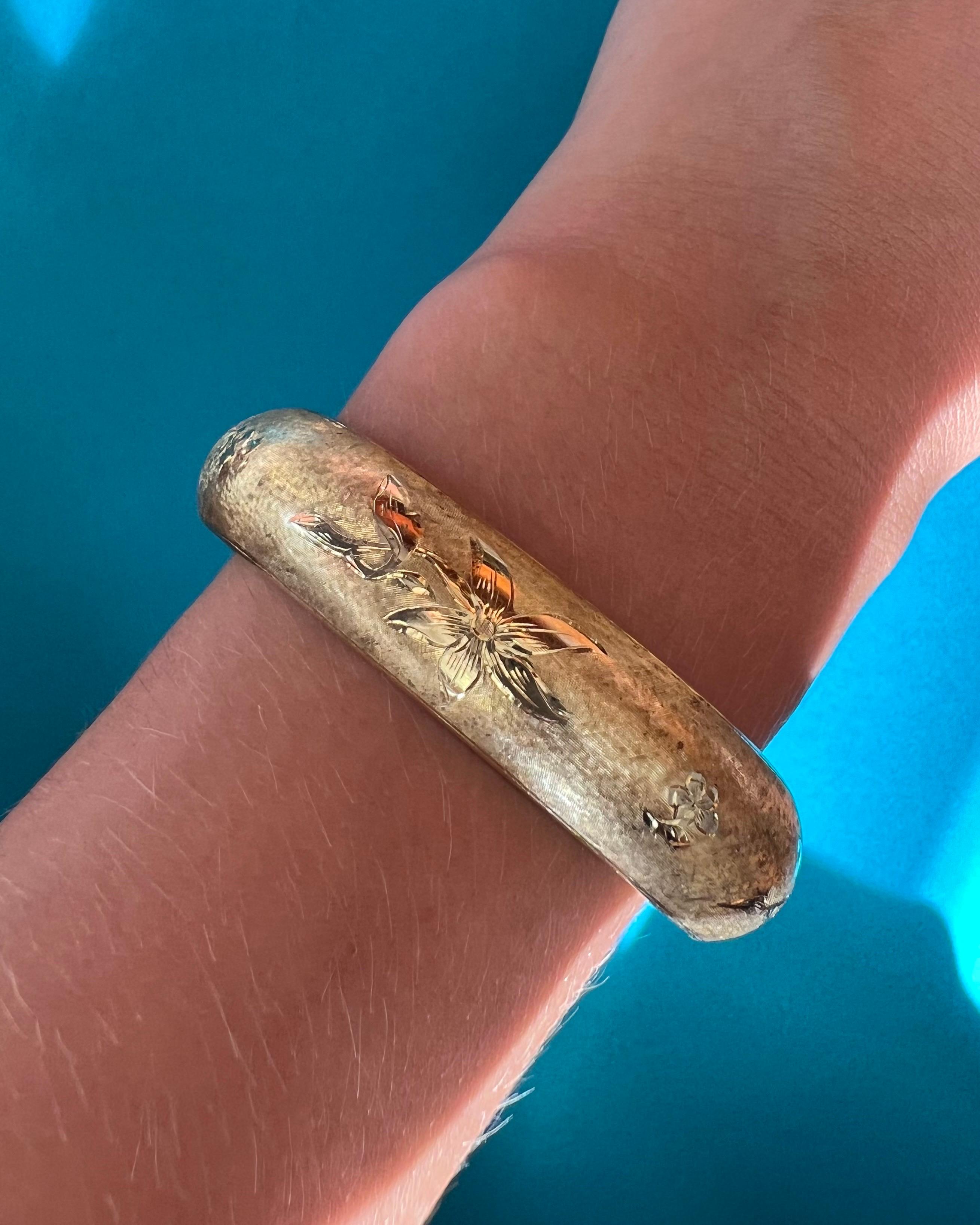 A vintage 14 karat gold bangle bracelet engraved with a lovely floral design. The gold surface of the bracelet is beautifully satined and engraved with a floral motif of stems and petals. The gold surface on the inner side is highly polished. The
