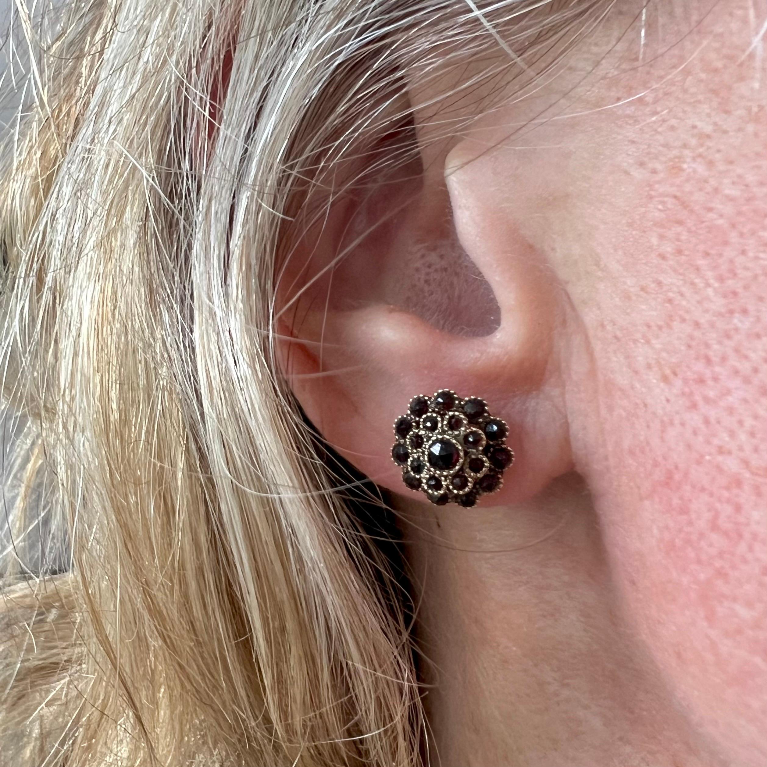A lovely pair of antique natural red garnet clustered stud earrings. These Dutch antique flower shaped studs are set with a cluster of many small garnets and are bezel set in a 14 karat gold mounting with a worked rim. The garnet stones have a