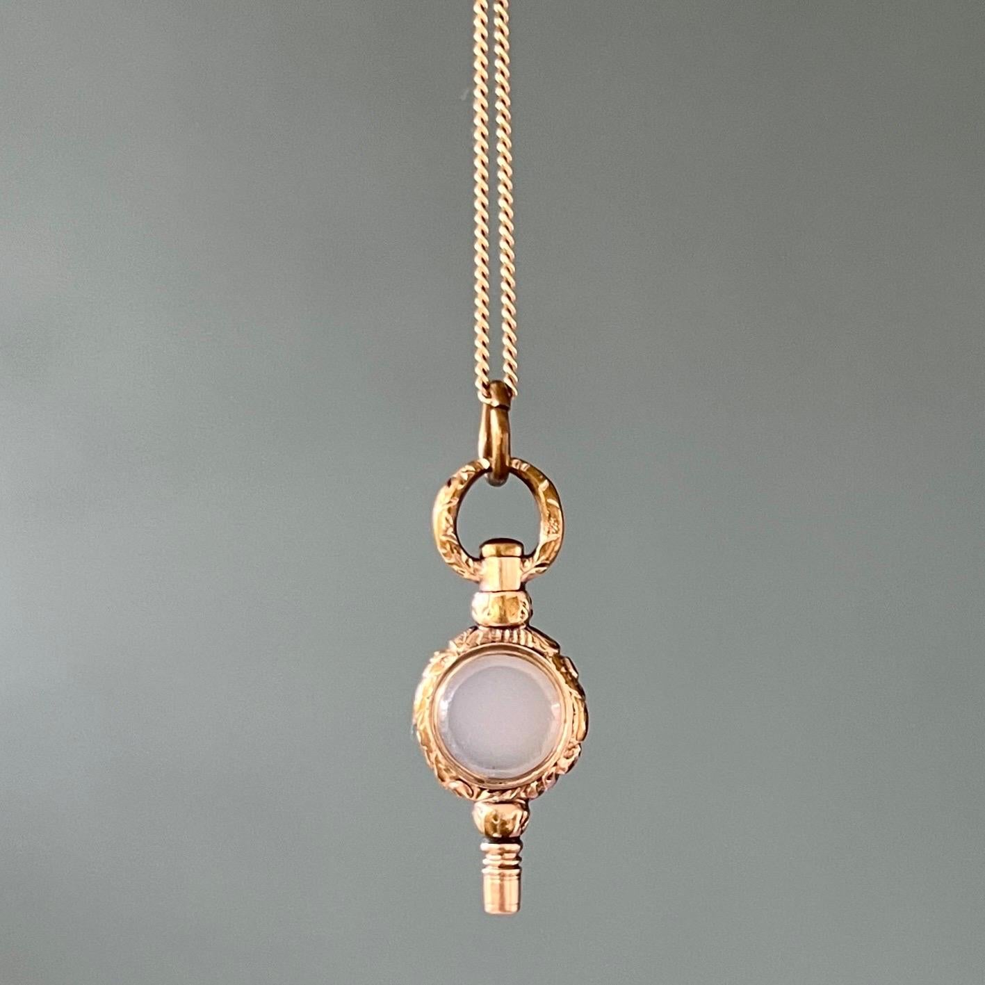 An antique Georgian 9 karat yellow gold pocket watch key charm pendant. This antique watch key has some great details. The key has a carved shank on top and the frame has a scrolling and chased design with a milky bluish colored agate stone in the