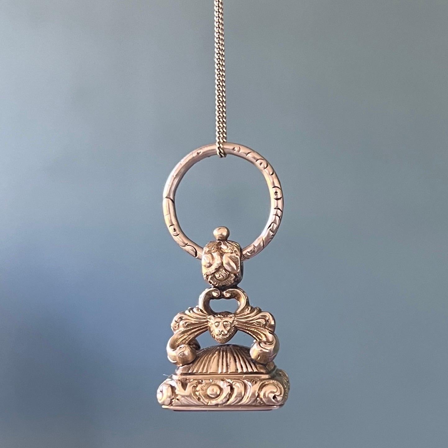 An antique early Victorian 15 karat gold and carnelian fob pendant. This beautiful ornate fob with lions head and scrolling arches leading to an integral bail attached to a gold split ring. The large split ring is embellished with deeply carved