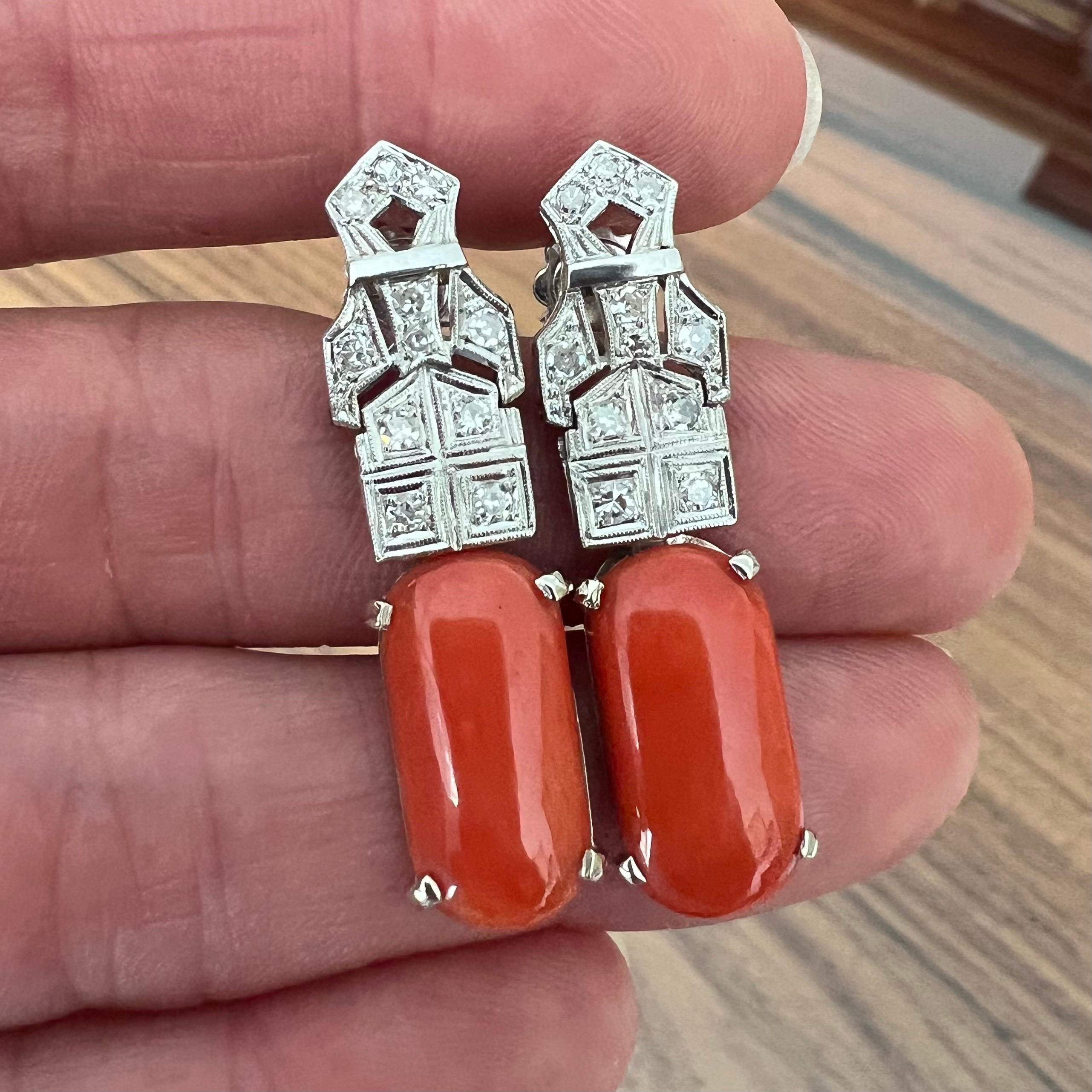A pair of 18 karat white gold and coral dangle earrings. The earrings are set with eleven octagonal cut diamonds with a dropper of a dark red coral cabochon. The earrings are made of 18 karat white gold with super clear diamonds of approximately