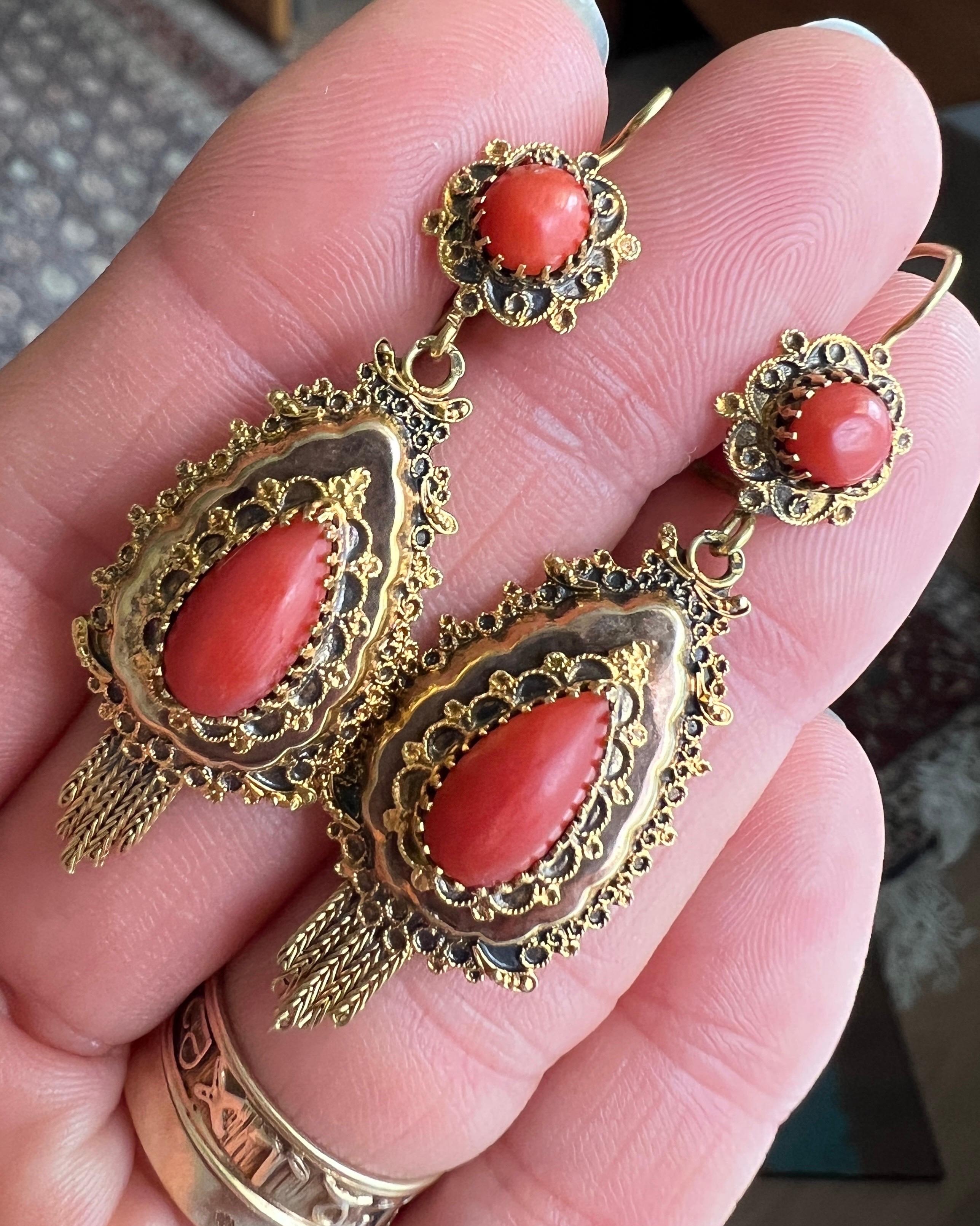 A vintage pair of natural red coral dangle earrings set in a 14 karat gold mounting. The earrings have a beautiful cannetille border inlaid with a red coral cabochon. Each earring has two coral cabochons cut stones, a smaller coral set in a rosette