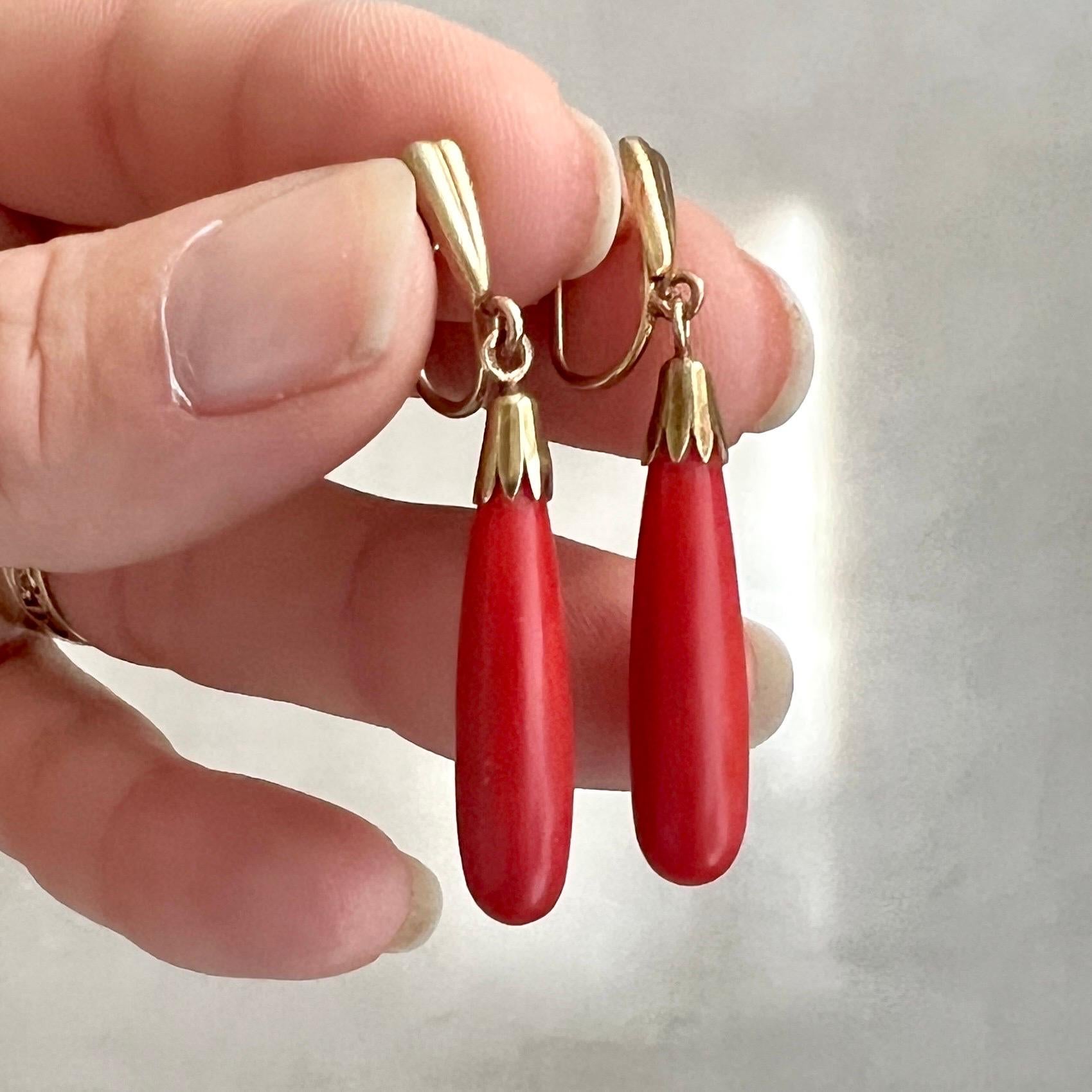 Lovely vintage 14 karat gold natural red coral dangle earrings. The pendant of the earrings are drop-shaped and the back is characterized by their secure back screw design. The design on the front side of the earrings is an Art Deco-style with