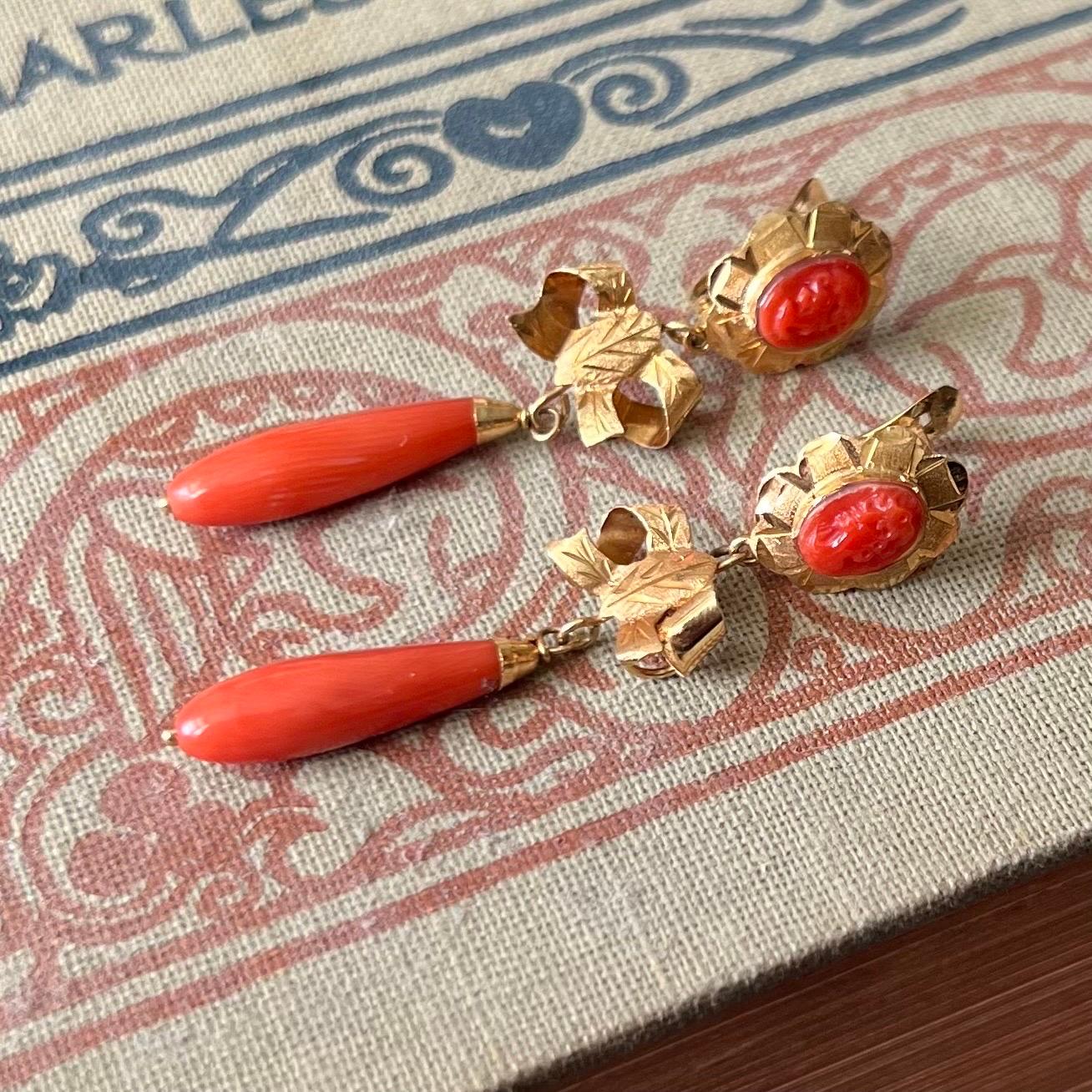 A fine and impressive pair of vintage coral and 18 karat yellow gold drop earrings. Each articulated earring features a signature torpedo-shaped coral drop. The coral drop is crowned with a yellow gold bow and hangs from an oval-shaped engraved