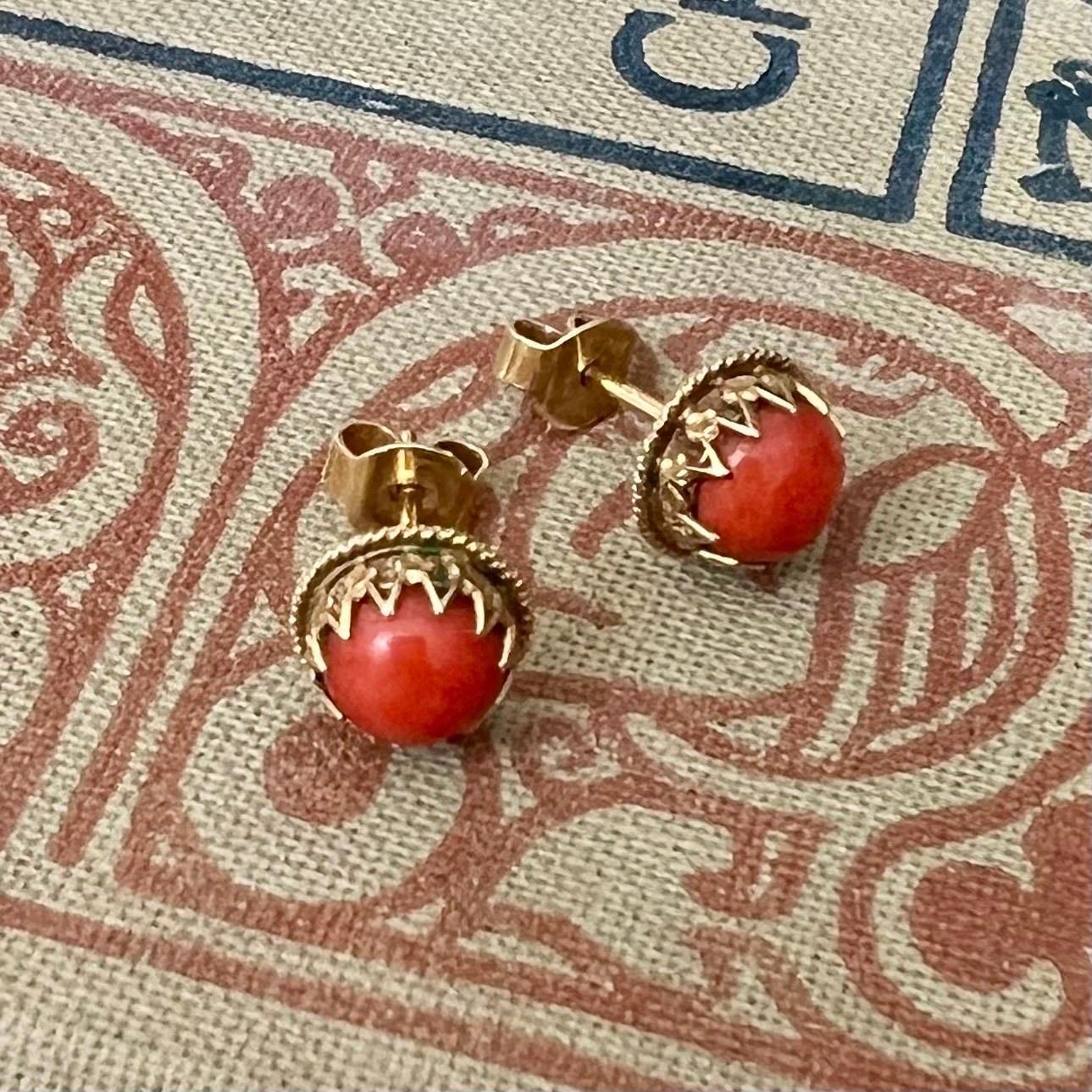 A gorgeous pair of antique red coral and gold stud earrings. The natural coral studs are bezel set in a 14 karat gold mounting. The gold mounting around the stones have a zigzag prong setting and rope decor. The studs are crafted with a round