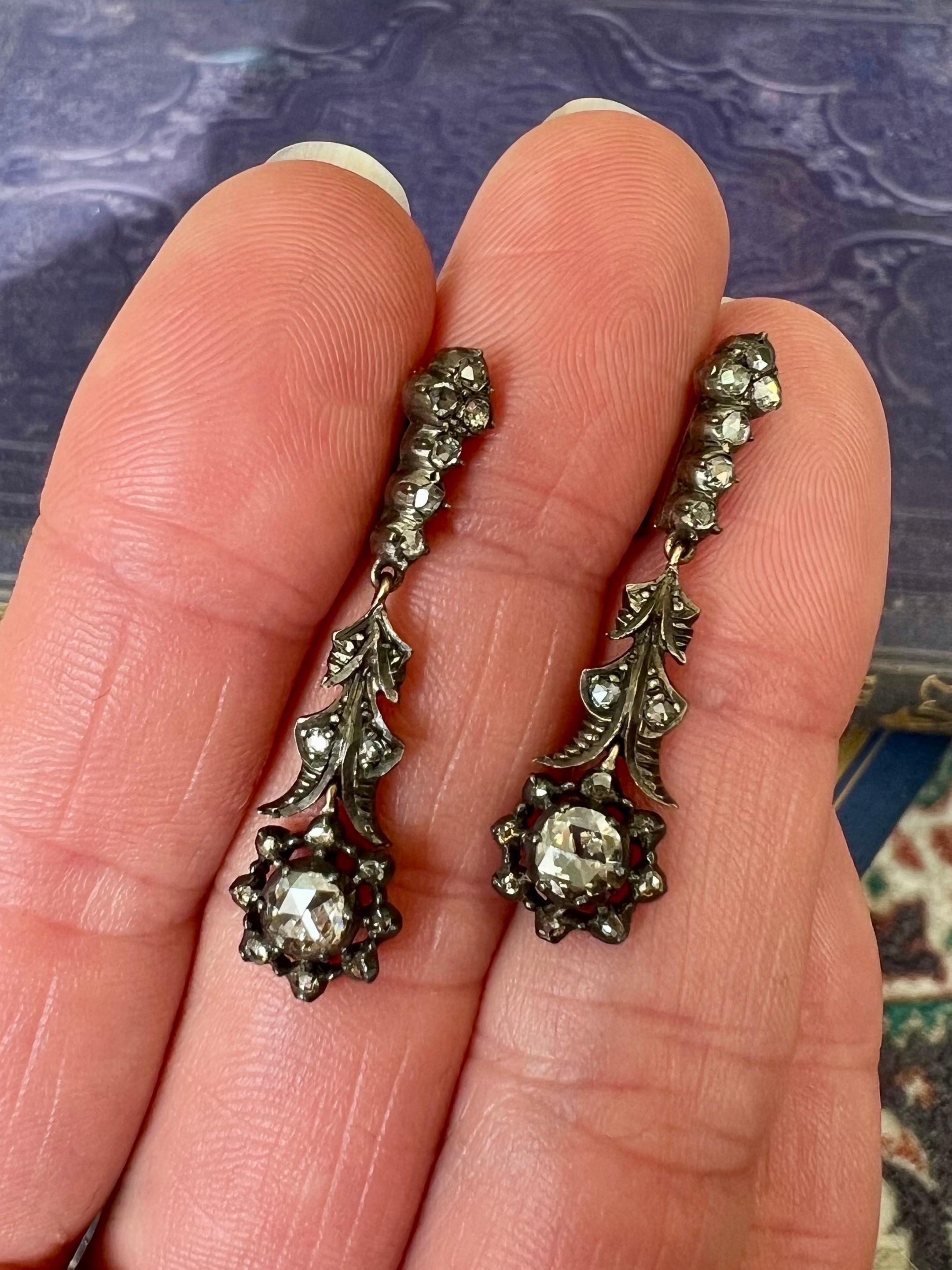 An antique 19th century pair of yellow gold earrings set with rose cut diamonds crafted in a silver setting. These antique Dutch dangle earrings have a beautiful design with leaves and a flower with a large diamond in the middle - while the stem and