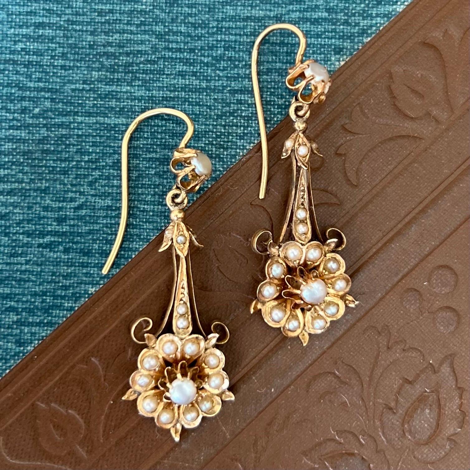 These late 19th century 14 karat gold dangle earrings are set with seventeen round pearls. The earrings are designed into a beautiful flower with leaves with an articulated frame structure. The flower has a cluster of lovely small seed pearls while