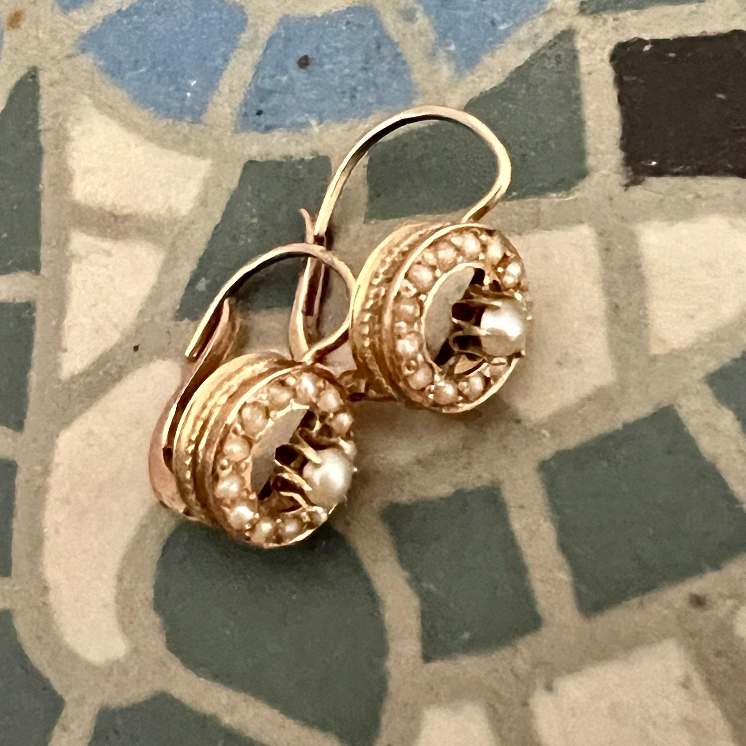 Antique 14 karat gold round drop earrings set with fourteen beautiful seed pearls. The round frame has an open structure with a pearl in the center of the earring studded with lovely seed pearls in the outer ring. The center pearl is larger than the