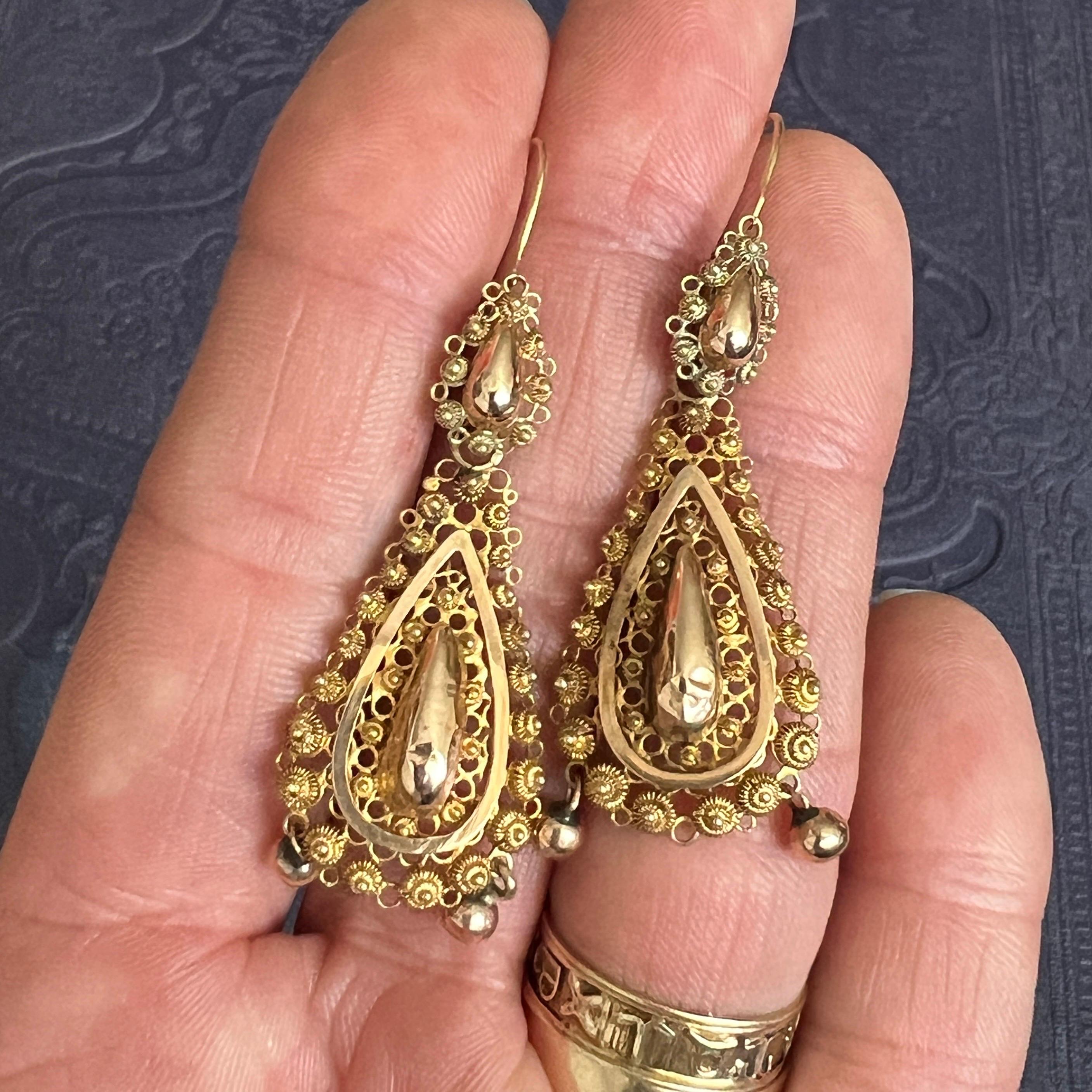 An antique pair of 14 karat gold dangle earrings crafted with a rich design of fine filigree and cannetille work. The earrings are beautifully made by hand with fine wirework and set with cannetille work which consists of small knots throughout the