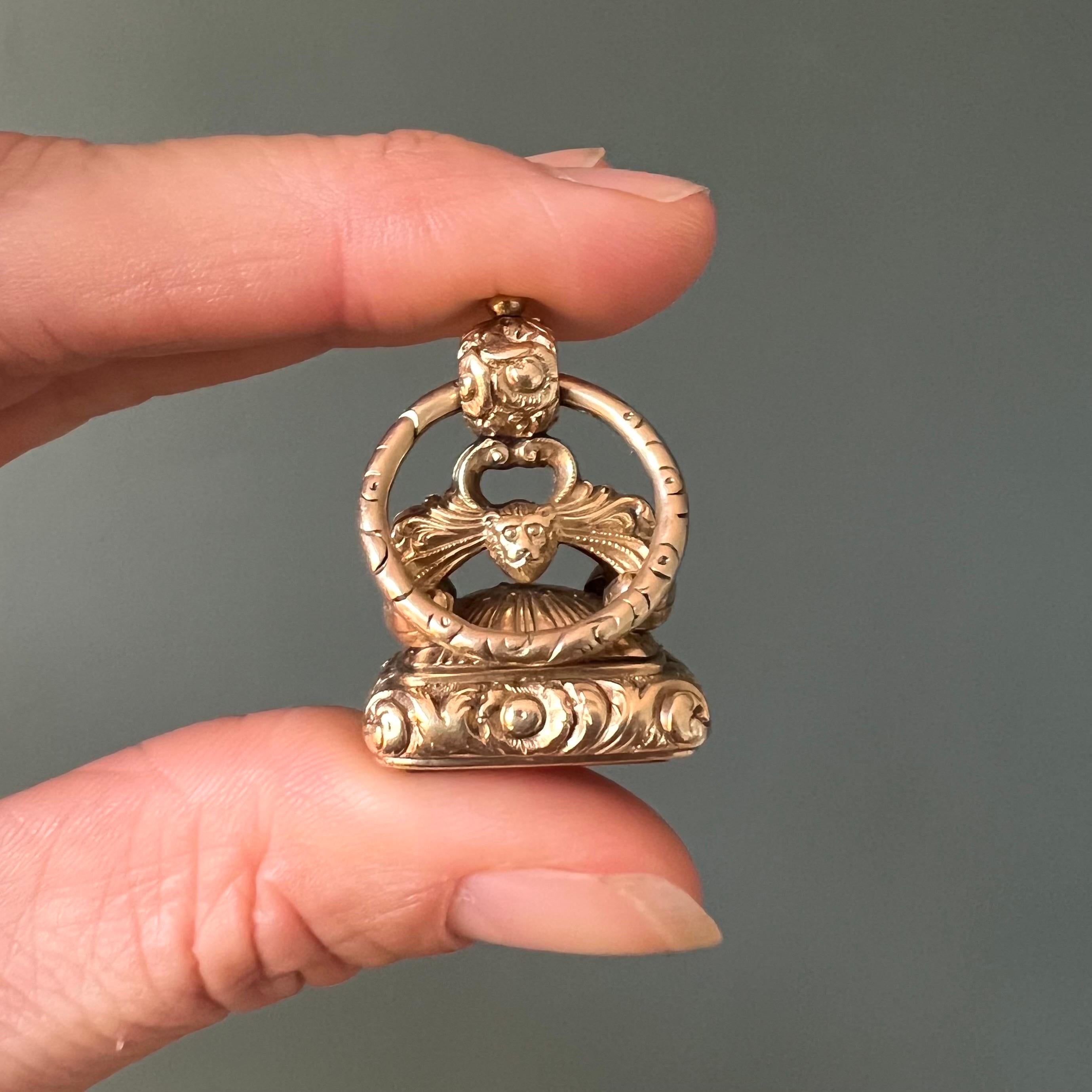 Antiguo colgante victoriano de oro de 15 quilates y cornalina, con una artesanía excepcional y gran riqueza de detalles. Esta ornamentada leontina presenta cabezas de león esculpidas y elegantes arcos que conducen a una fianza integral, unida a una