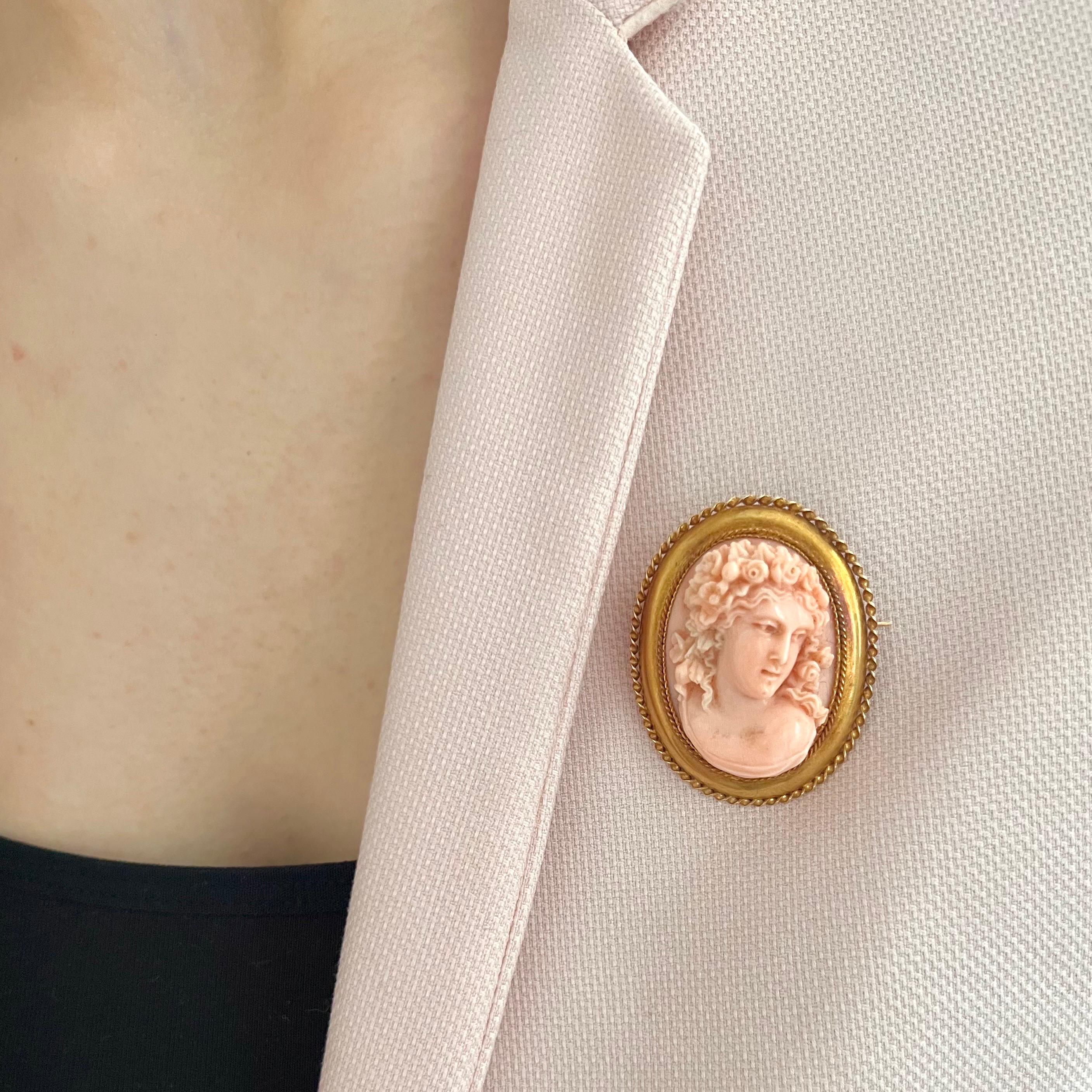 Este hermoso broche antiguo presenta un camafeo de coral finamente tallado que representa a Flora, la diosa romana de las flores y la primavera, representada en sorprendente altorrelieve. Su expresión serena, su cabello que fluye delicadamente