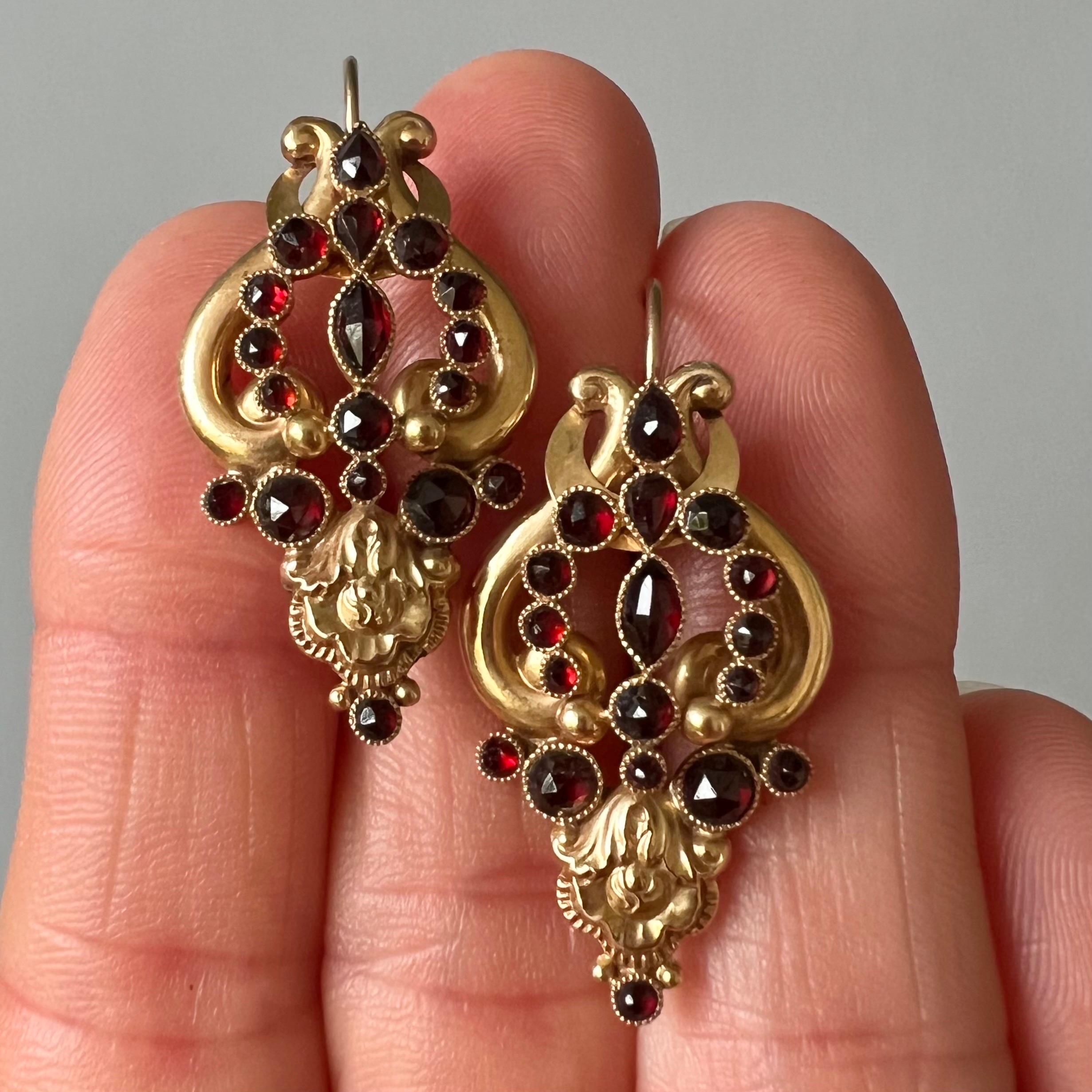 Eleganti orecchini in oro 18 karati repoussé con volute e articolazioni, risalenti all'inizio del XIX secolo. Il design ricorda l'arpa a lira ed è incastonato con bellissimi granati sfaccettati. I granati hanno diversi stili di taglio - ovale,