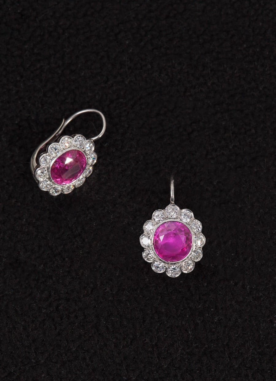 Original Edwardian rosette earrings each centering 1 bezel-set oval mixed-cut ruby surrounded by 12 old European-cut diamonds completed by a wire-lever back closure. The rubies weigh 3.25 carats and 3.27 carats and are accompanied by a *GUBELIN