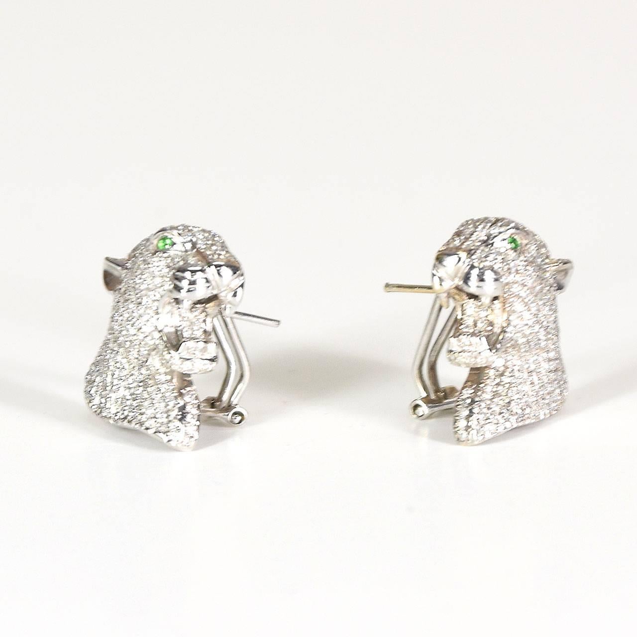 After Cartier, modelled as panther heads, each earring is pavé set with round brilliant cut diamonds, all totalling 3.31cts.  Each panther has green garnet-set eyes, secured by hinged clip fasteners for pierced ears in 18ct white gold.  Calculated