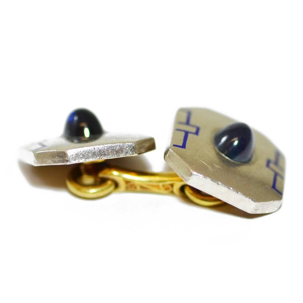 A pair of platinum cufflinks, each set with a cabochon sapphire and decorated with blue enamel detail.