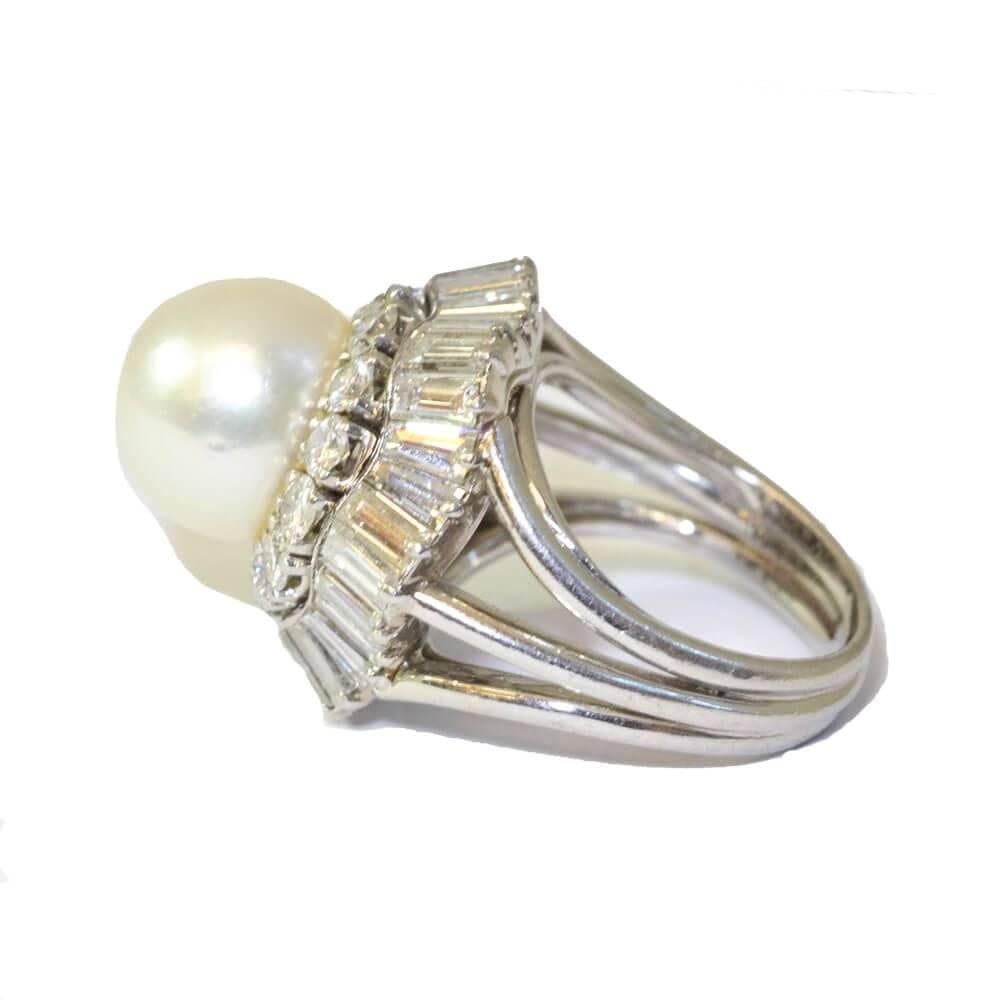 A cultured salt-water pearl and diamond cluster ring, having two rows of diamond surround, one with brilliant cut diamonds and one with multiple baguette cut diamonds forming an undulating  ‘skirt’. Mounted in platinum. French, circa 1940.
Ring size