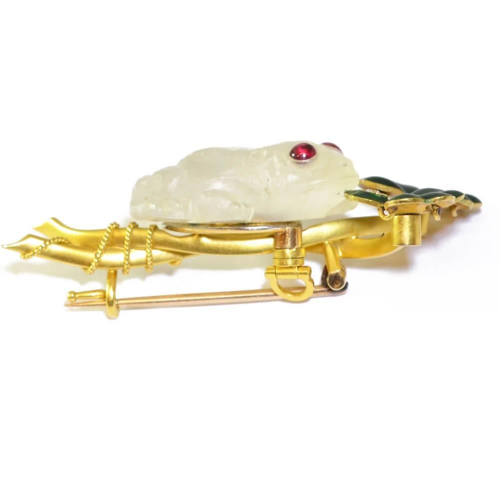 A brooch in the form of a carved moonstone frog with ruby eyes on a spray of green enamel clover with diamond dew drop. Mounted in yellow gold. American, circa 1900.